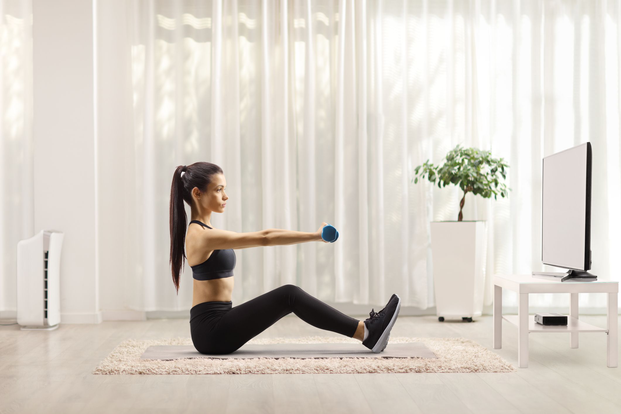 Young woman exercising with dumbbells in front of a tv at home