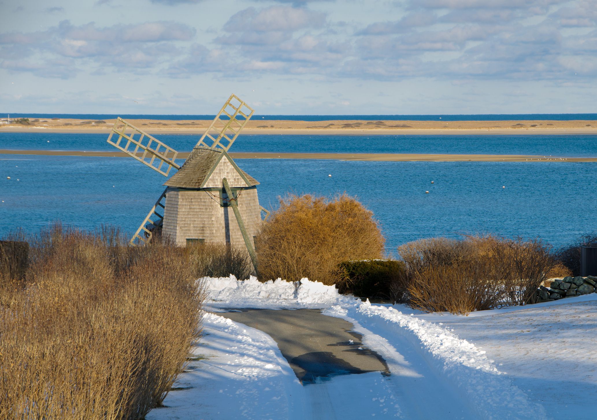 A snow covered roadway leads to an old windmill at the edge of a bay on Cape Cod