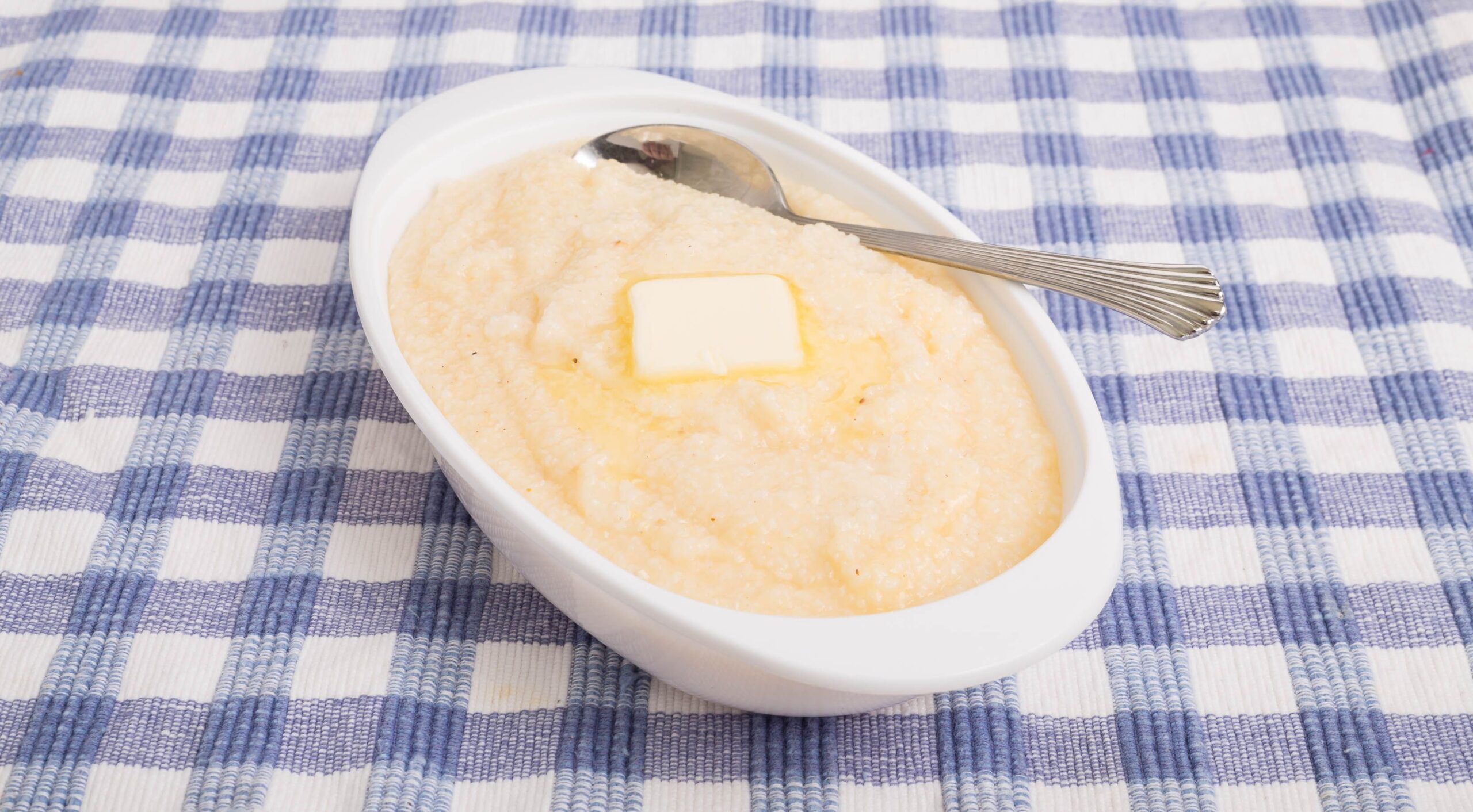 A bowl of white corn grits on a blue plaid placemat