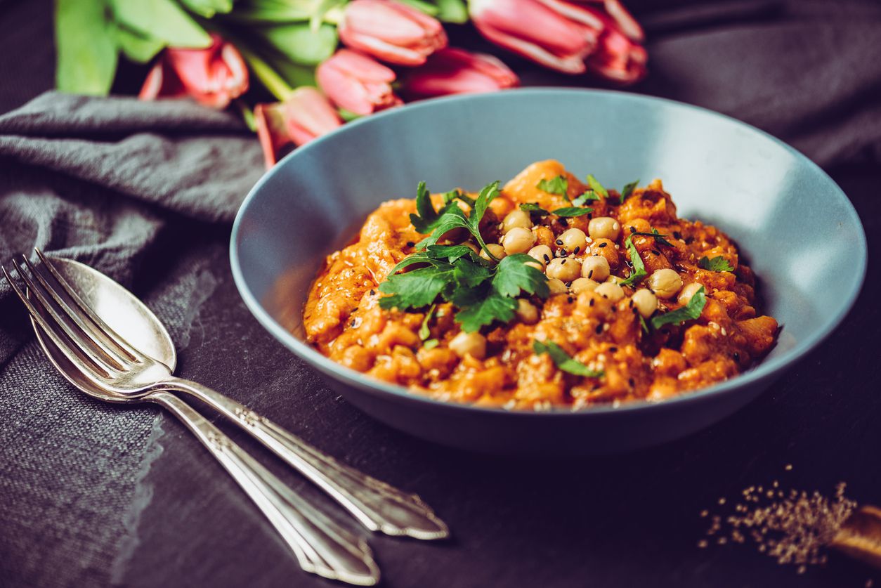 Chana Alu Masala in a blue gray bowl on a black table cloth with cut red tulips