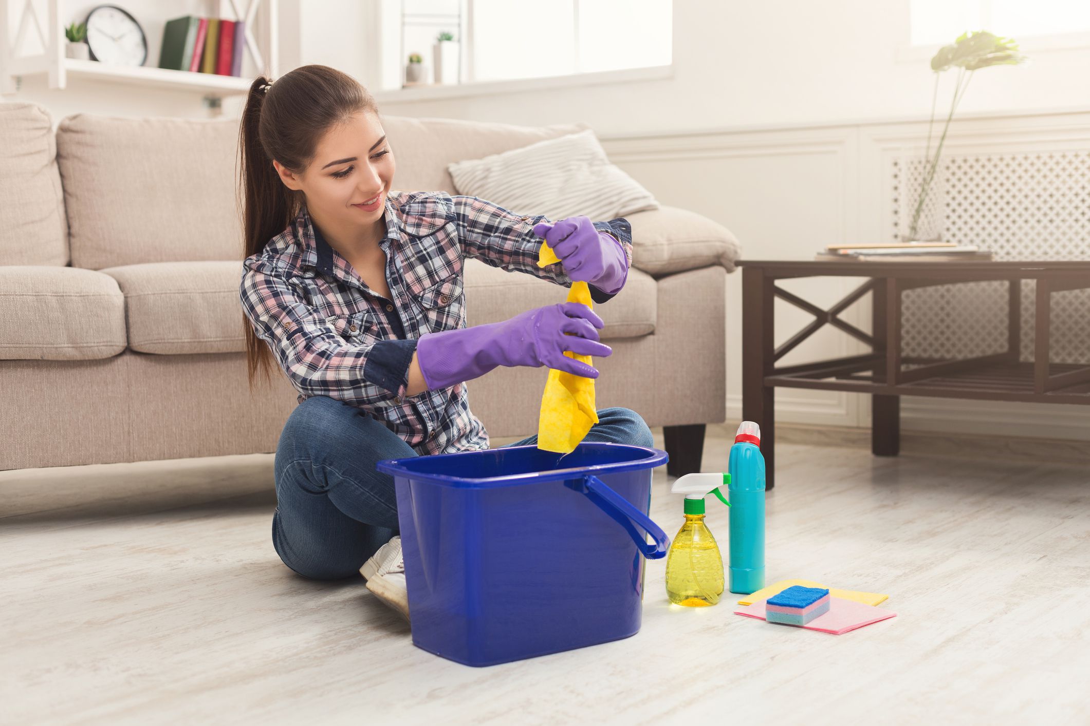 Young woman winkling out towel, tired of spring cleaning house, washing floor with rag, bucket and detergents, copy space