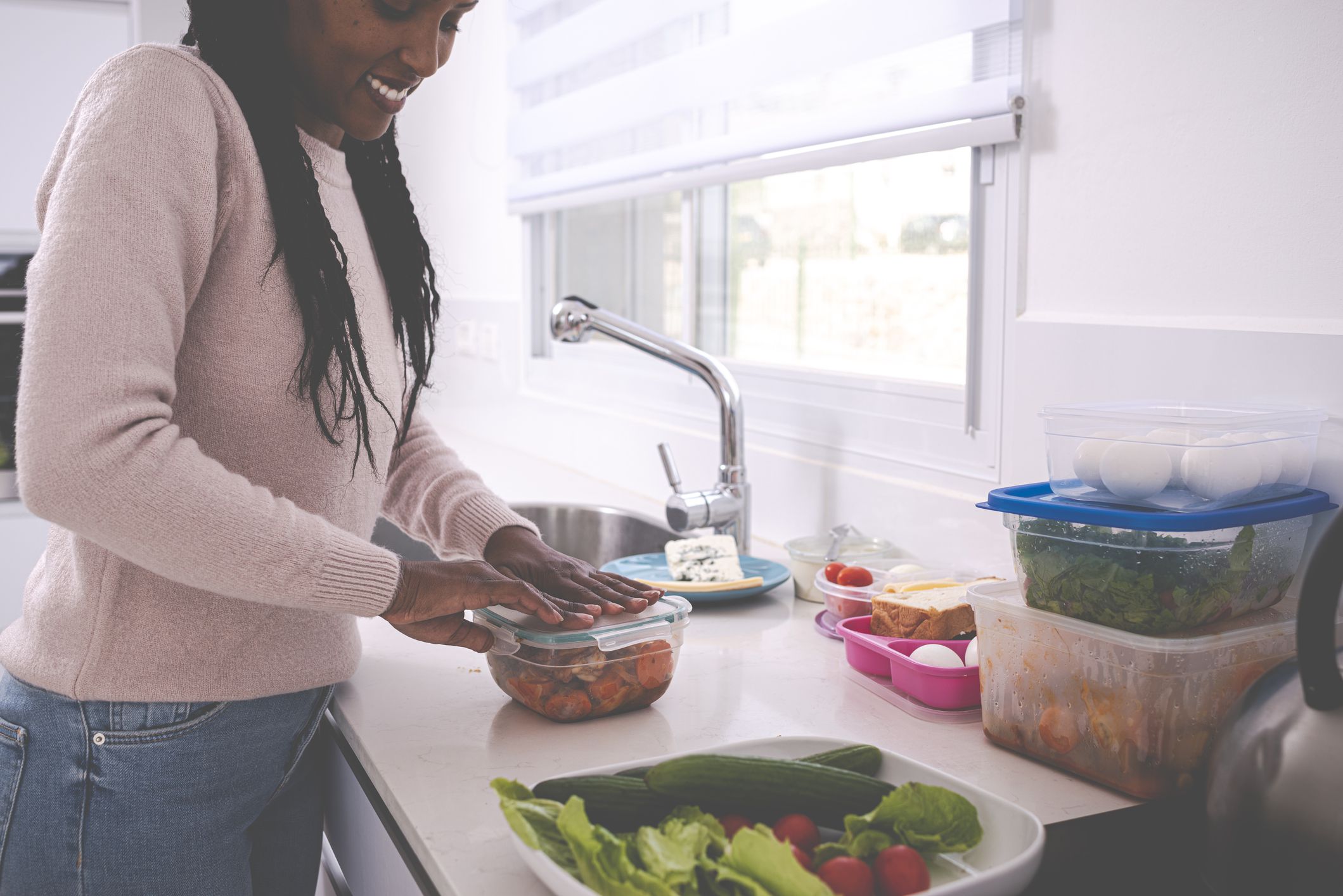 A young woman packing leftovers into a plastic container, cooking at a domestic kitchen.