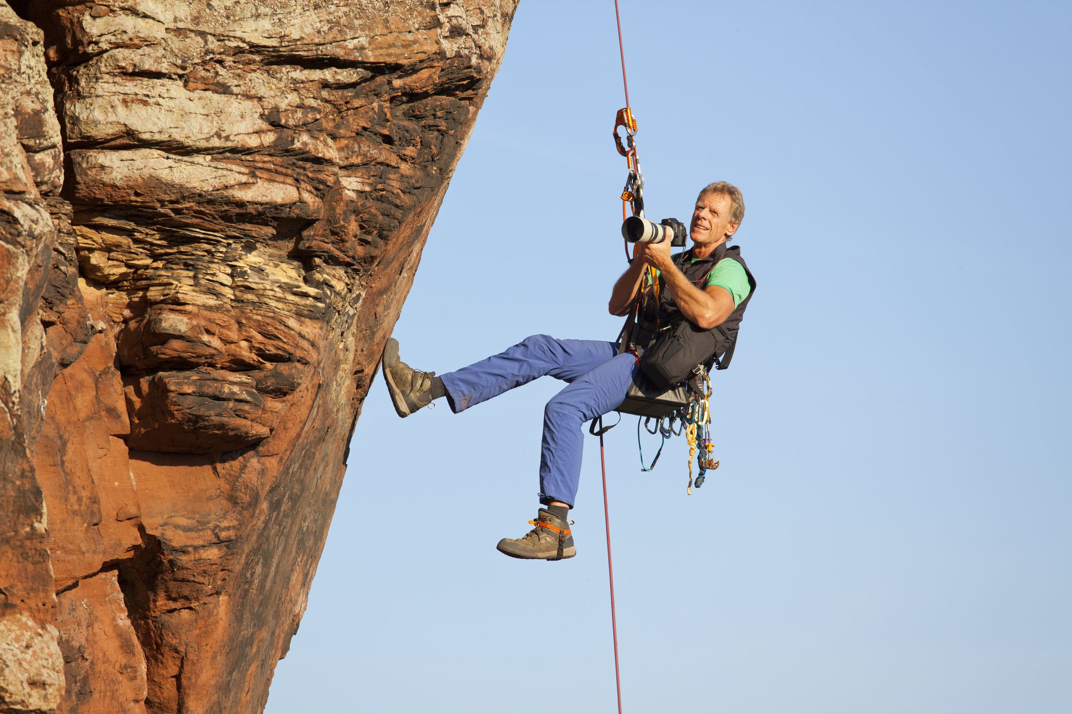 Photographer and rock climber Norbert Frank taking pictures while hanging in front of a rock