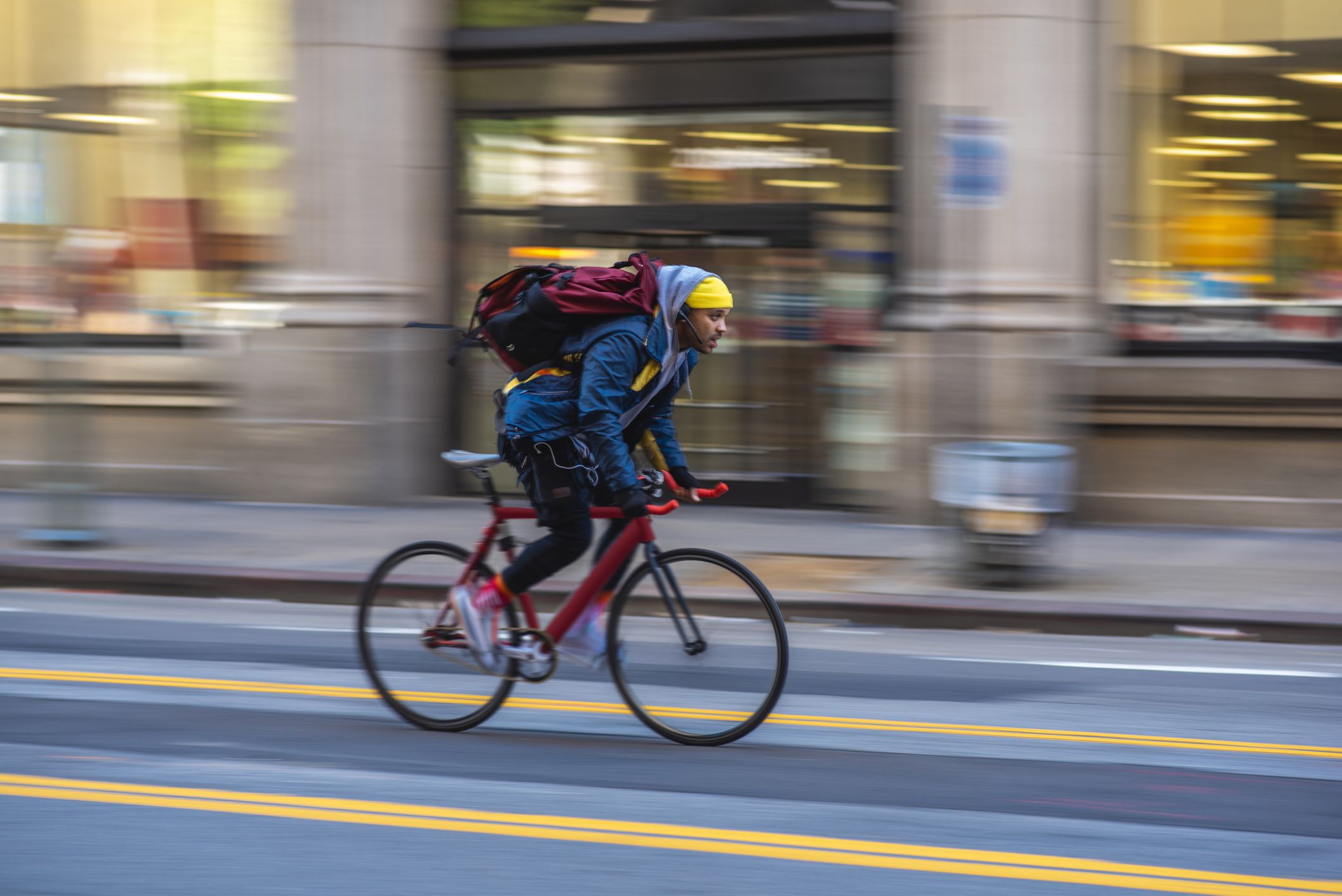 Blurred motion side view of biker in early 30s wearing backpack and moving past camera on downtown street in Los Angeles.