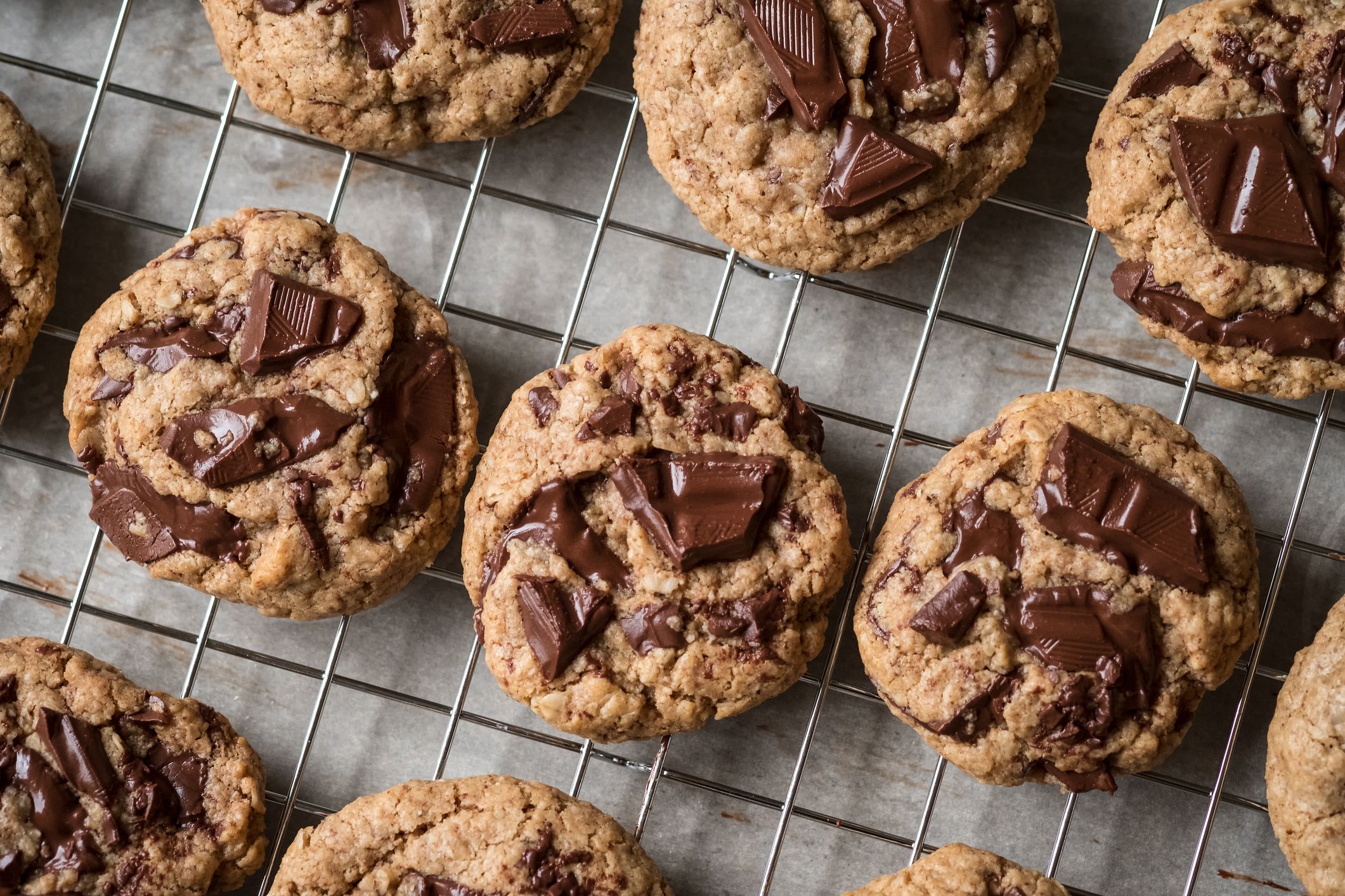 Rows of homemade dark chocolate chip cookies made with healthy vegan ingredients: oat flour, almond flour, almond butter, almond milk, and chopped dark chocolate. Fresh from the oven with chocolate melting.
