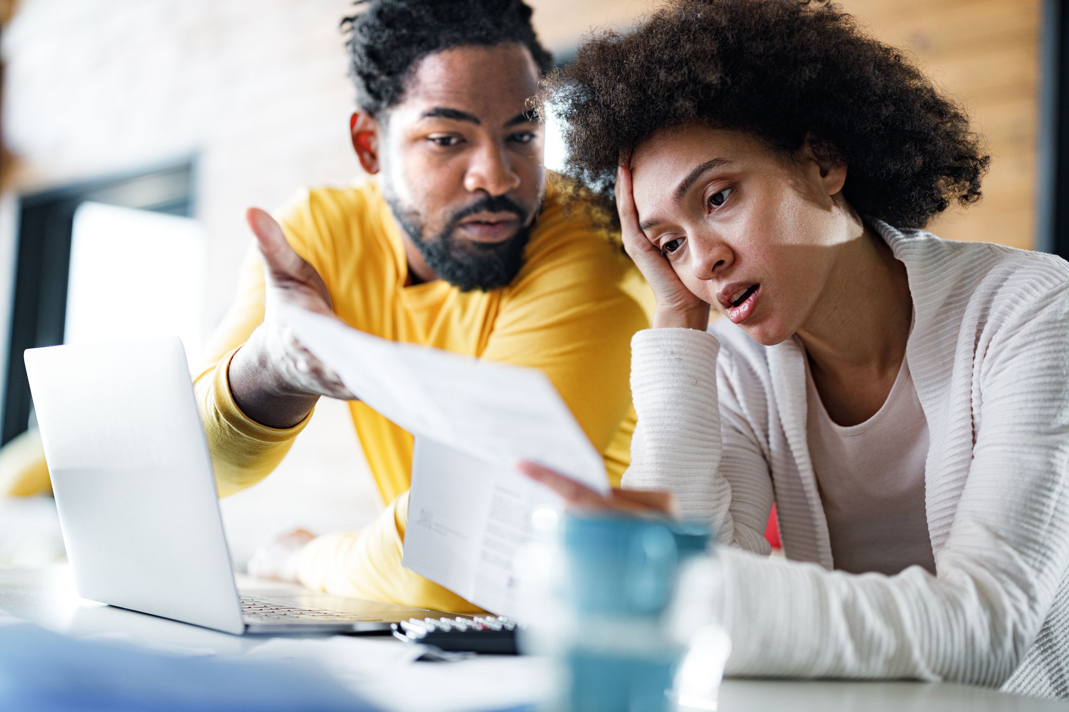 Young African American couple feeling frustrated while paying their bills over laptop at home. Focus is on woman.
