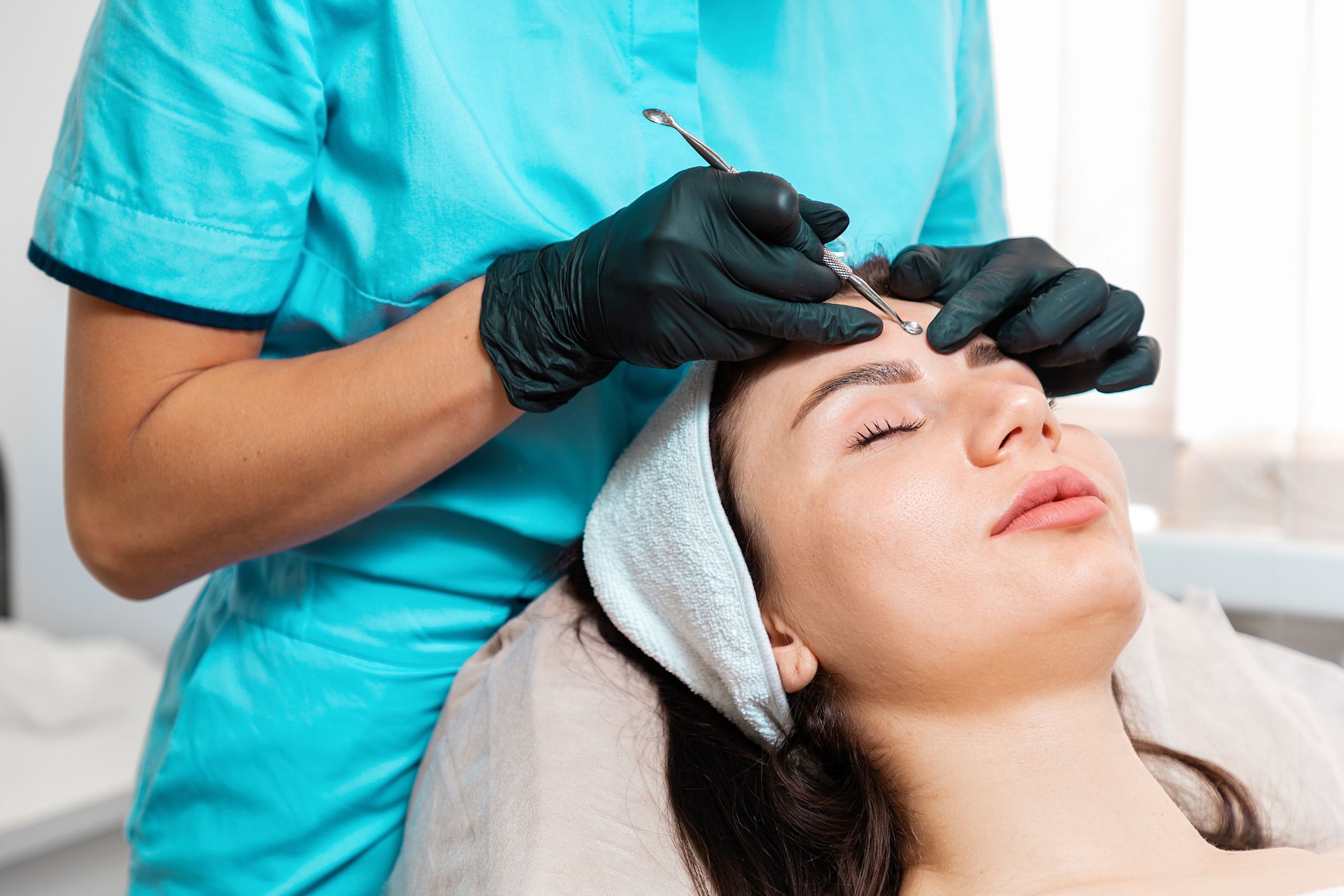 Professional cosmetology. Beautician doing blackhead treatment using mechanical steel tool. Close up of face. Concept of cleansing acne procedure.