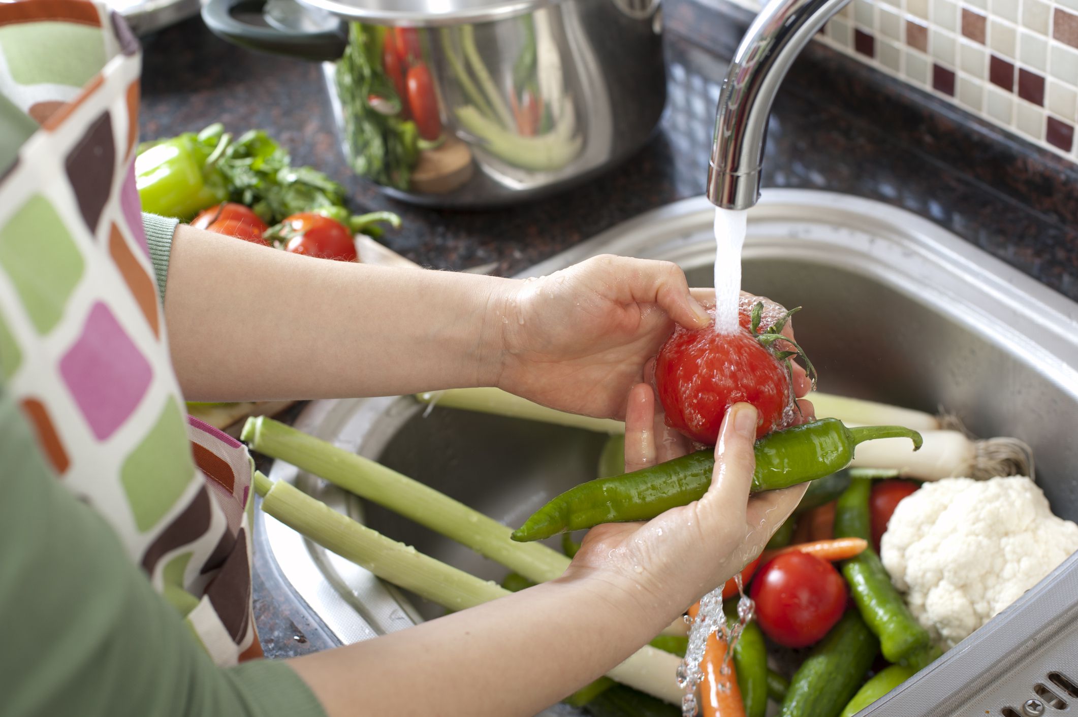 Woman washing vegetables in kitchen close up.