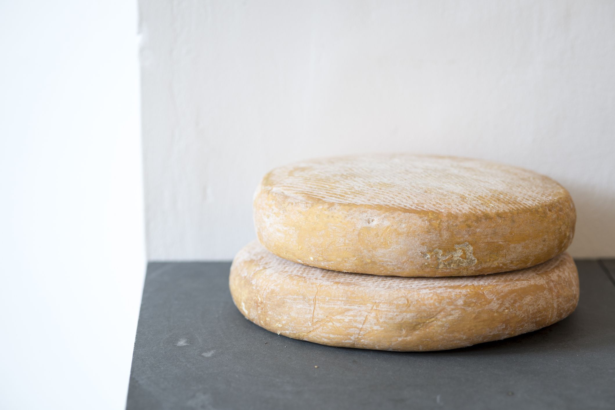 Two Durrus cheese rounds on slate against a painted white wall