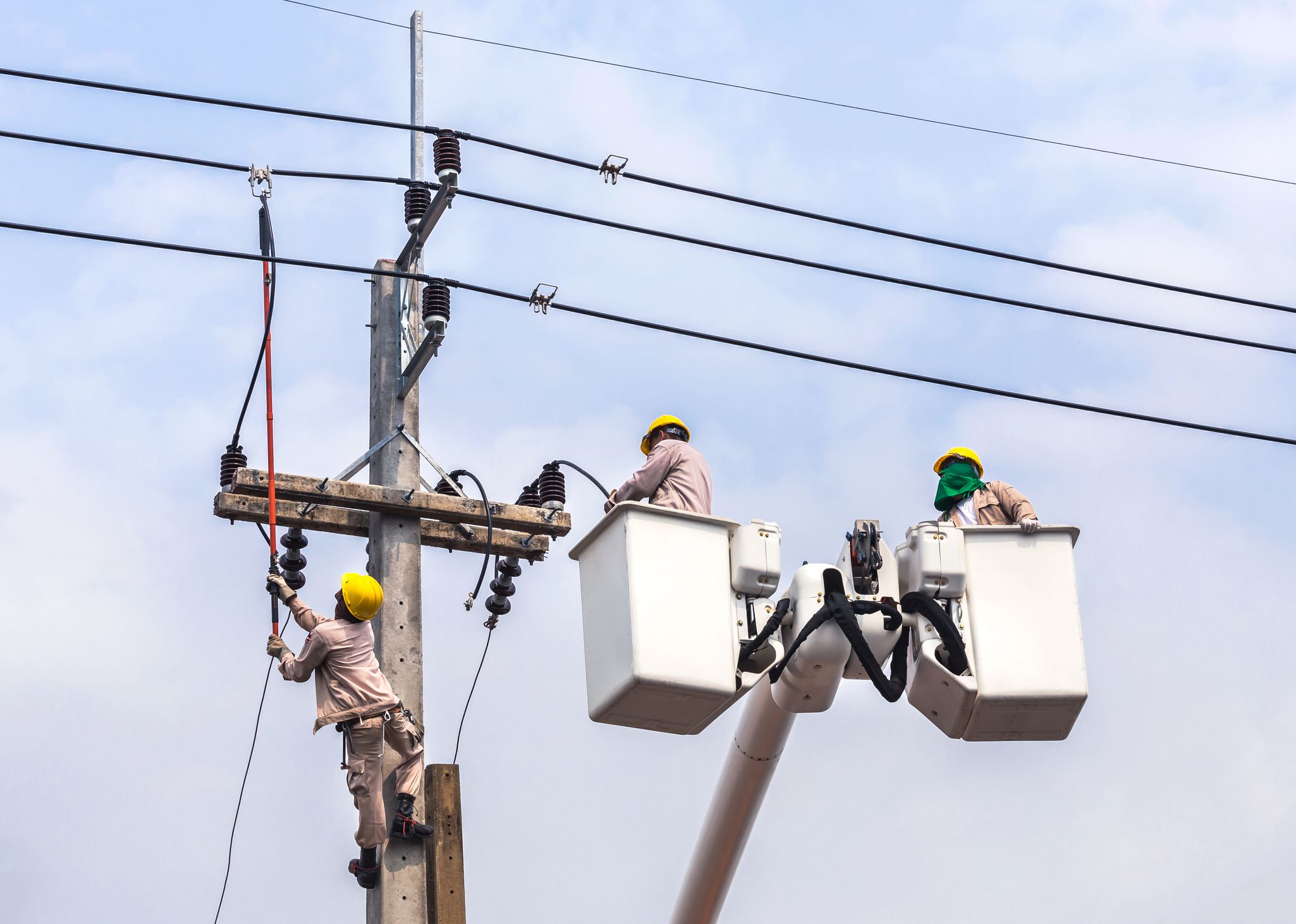 Electricians repairing wire of the power line with bucket hydraulic lifting platform on blue sky background