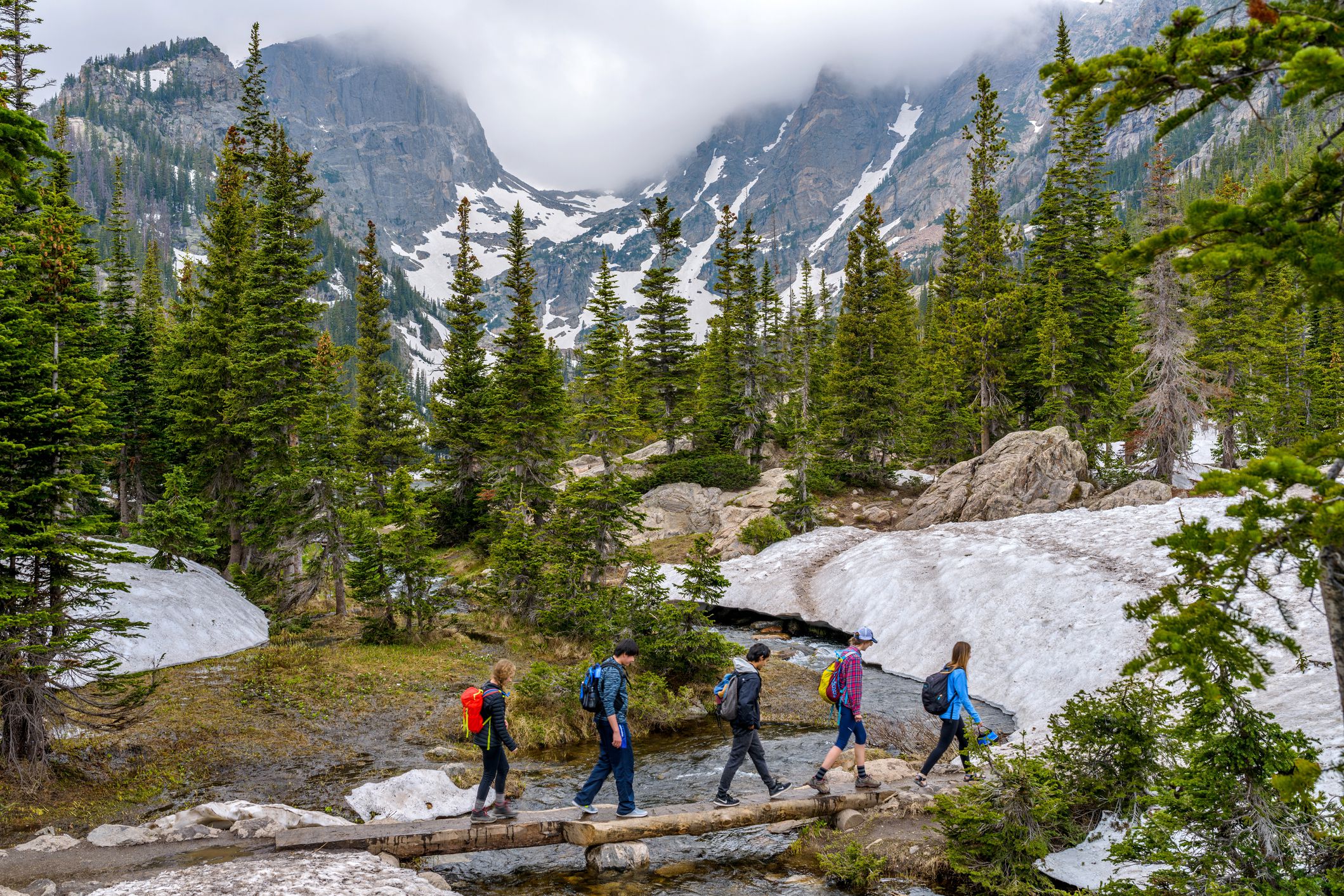 Estes Park, Colorado, USA - June 24, 2017: On a foggy spring day, a group of hikers walking cross a tree trunk bridge over Tyndall Creek on Emerald Lake Trail at base of Hallett Peak and Flattop Mountain in Rocky Mountain National Park.