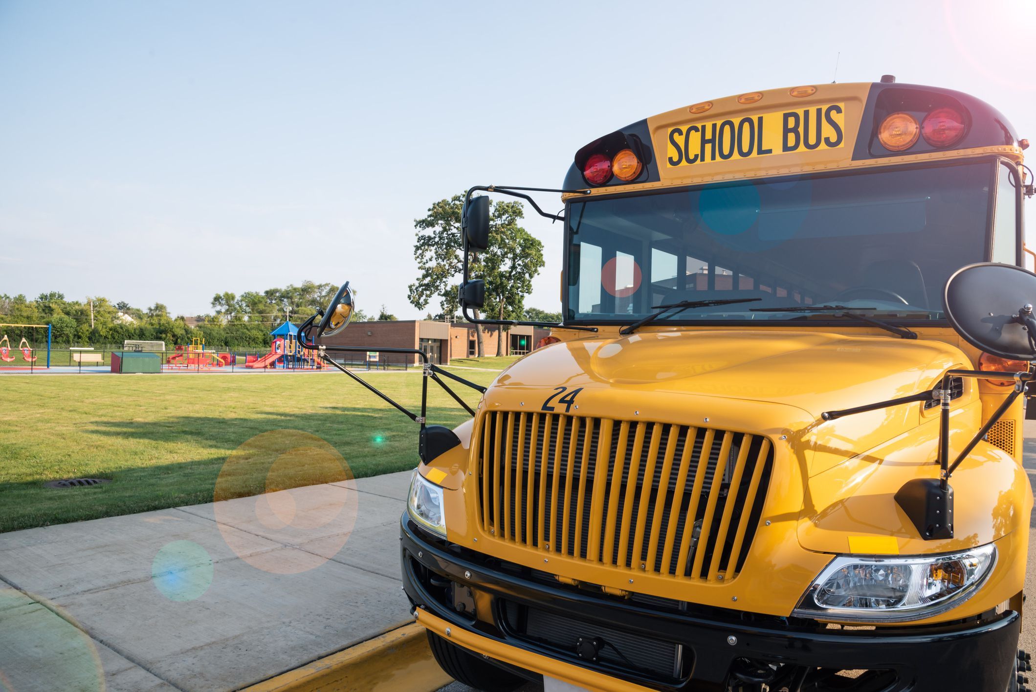 Closeup of a yellow school bus parked in front of a school playground with the school in the background