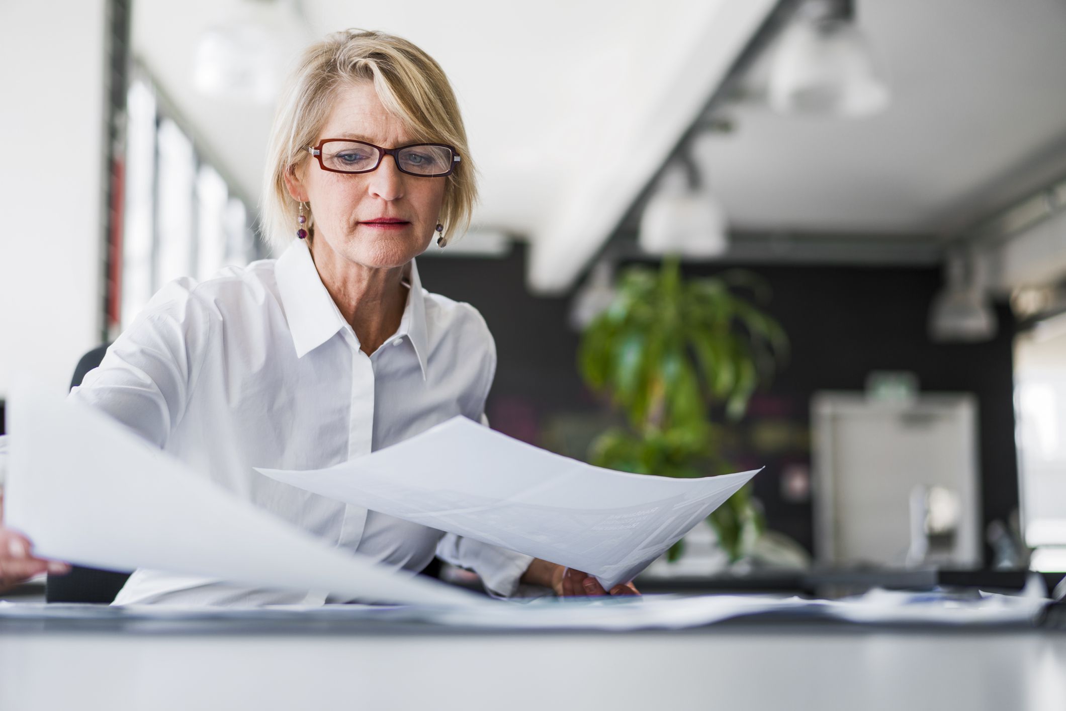 Focus on a senior businesswoman looking through documents with a blurred background of an office