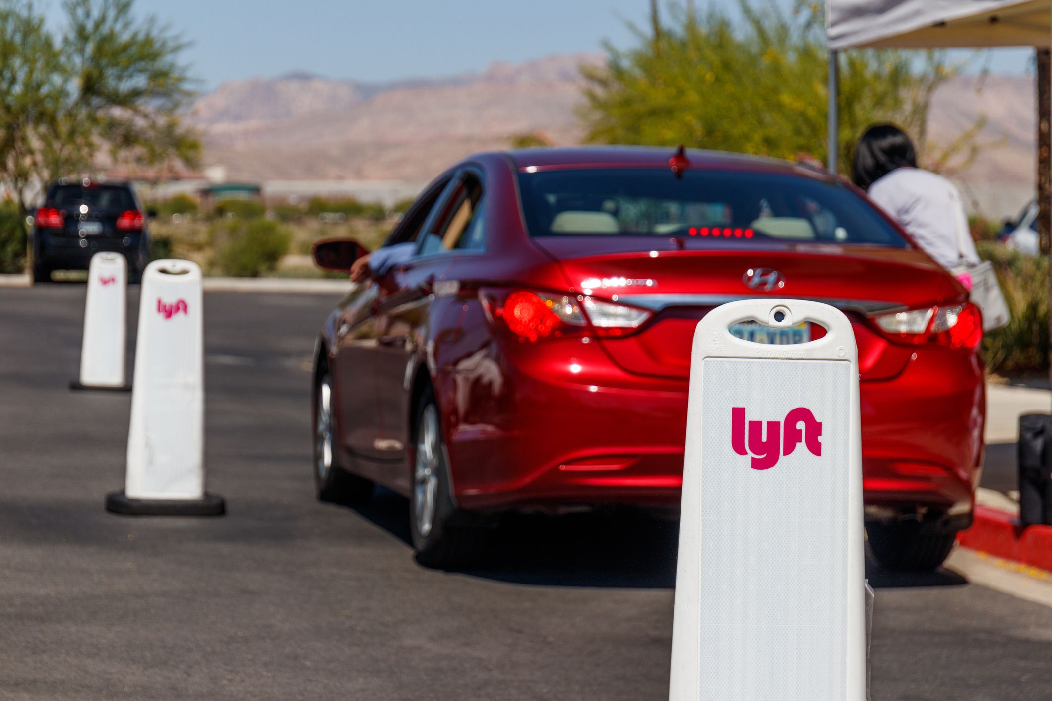 One red car with a person getting inside, in a Lyft Las Vegas Hub with mountains in the background