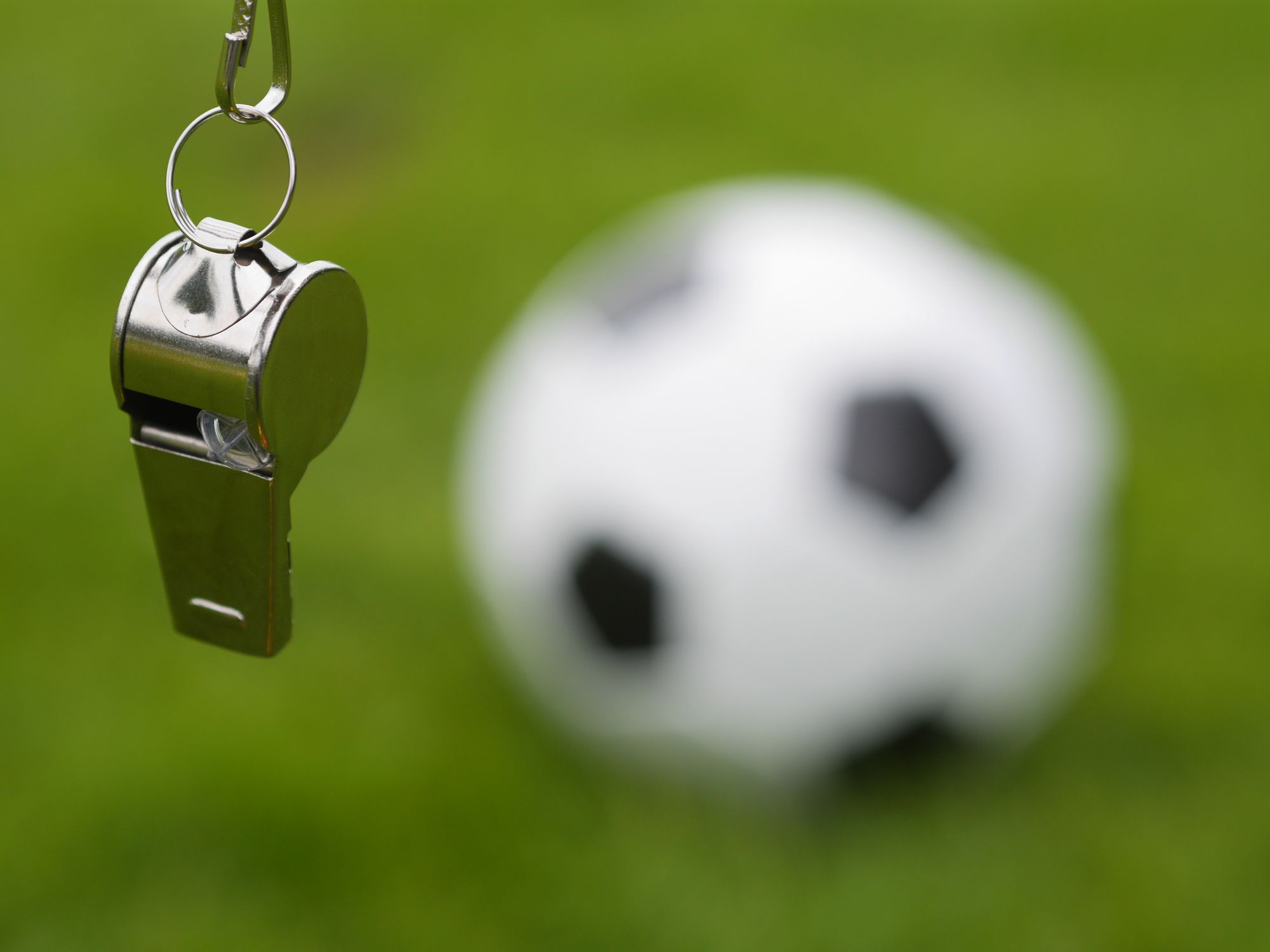Referee whistle hanging in front of a blurred soccer ball on field