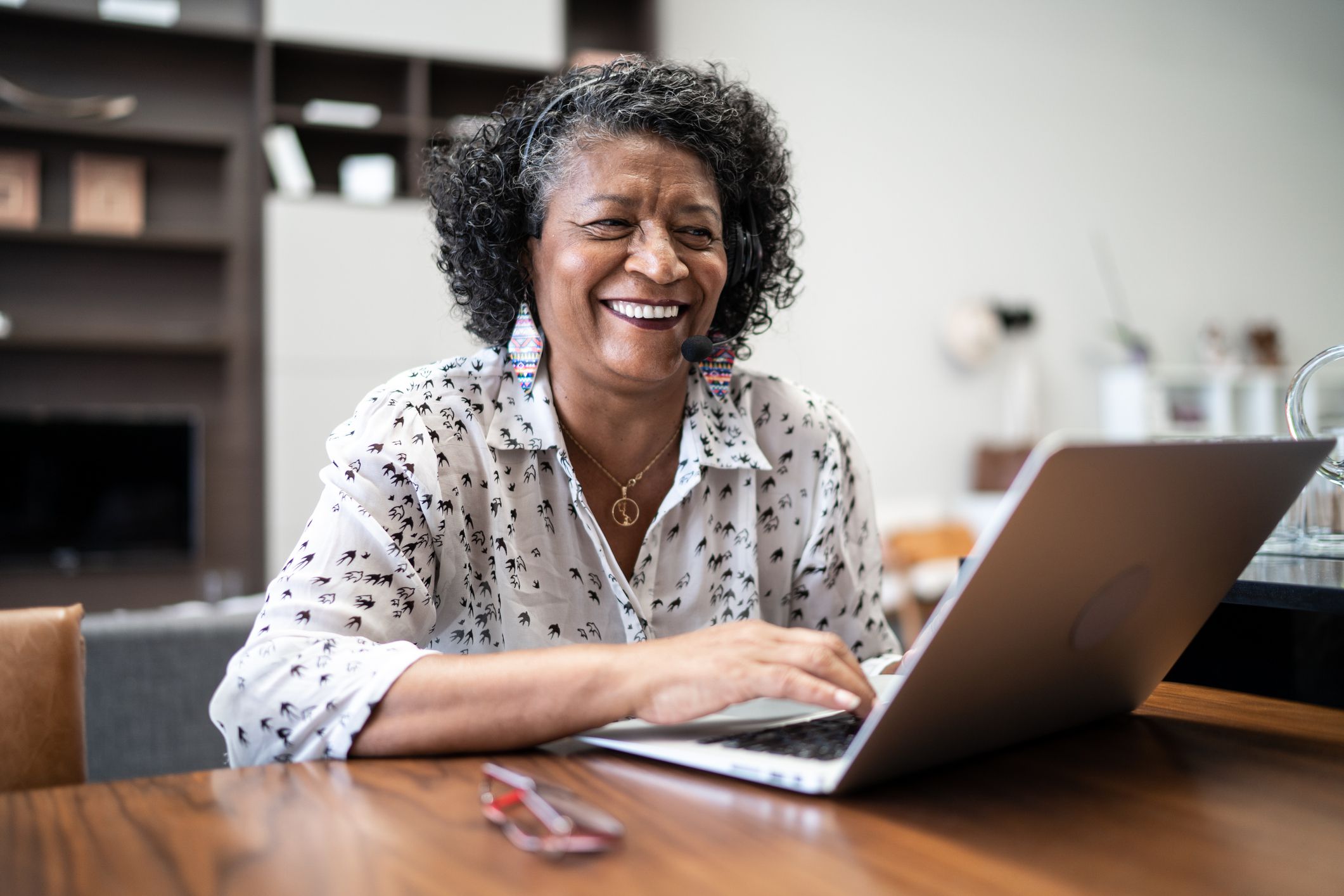 Senior woman working remotely on a laptop on her kitchen table at home with a blurred background of her kitchen