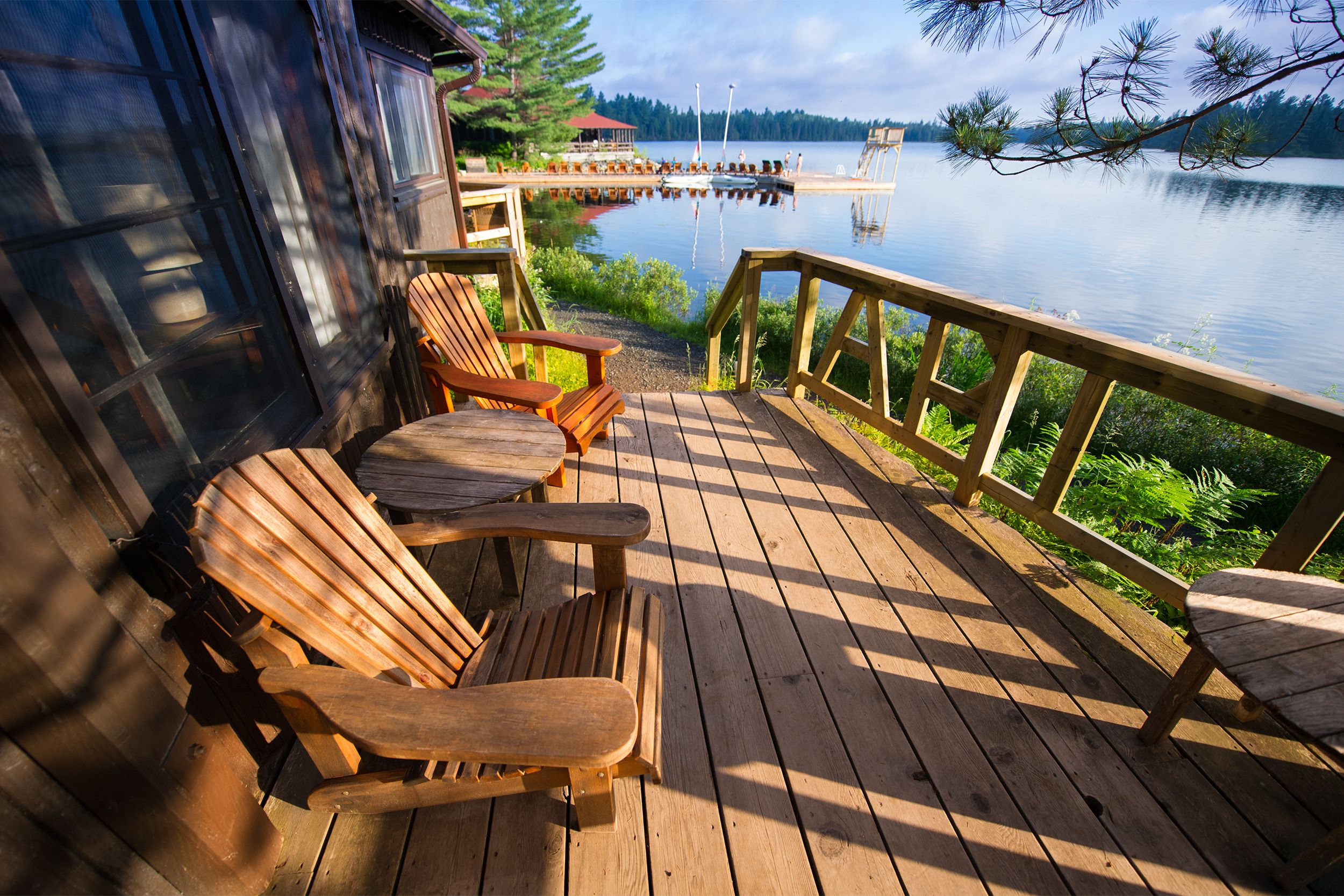 Two wooden rocking chairs on the wooden back porch of a lake house during summer with the lake and a small boat area in the background