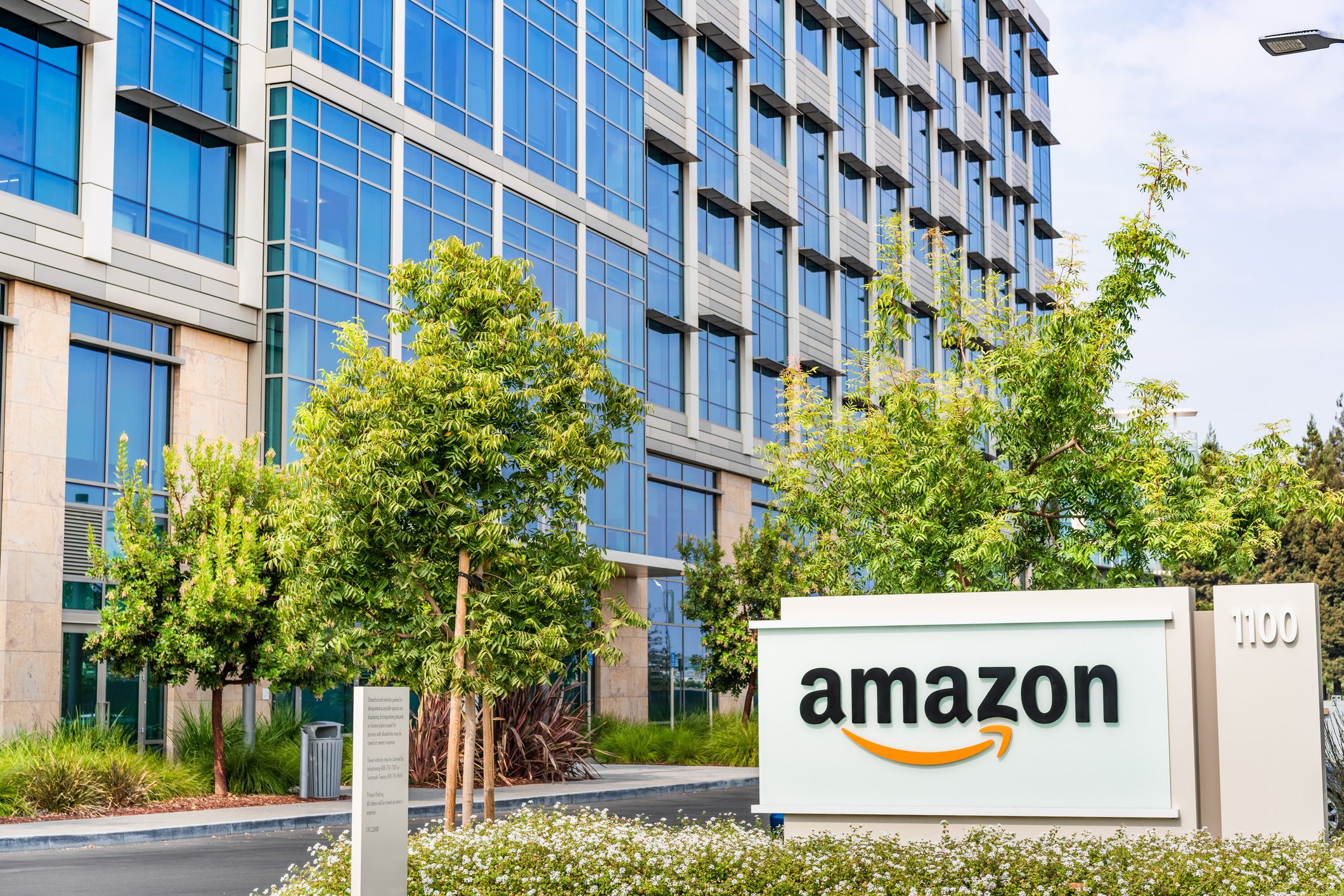 Sign with Amazon logo next to large Amazon office building.