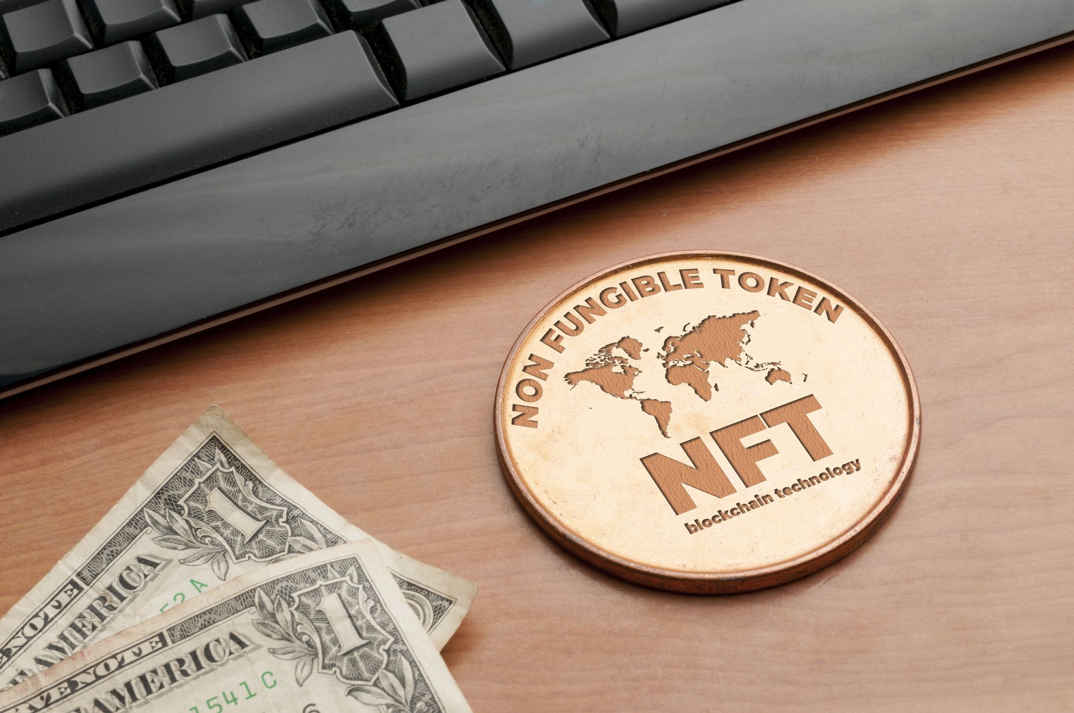 Nft (non fungible token) concept: big copper coin on a wooden table with a computer keyboard and two dollar bills
