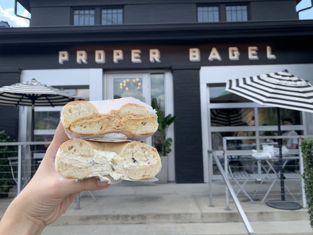 Proper Bagel bagel being held in front of outside door sign