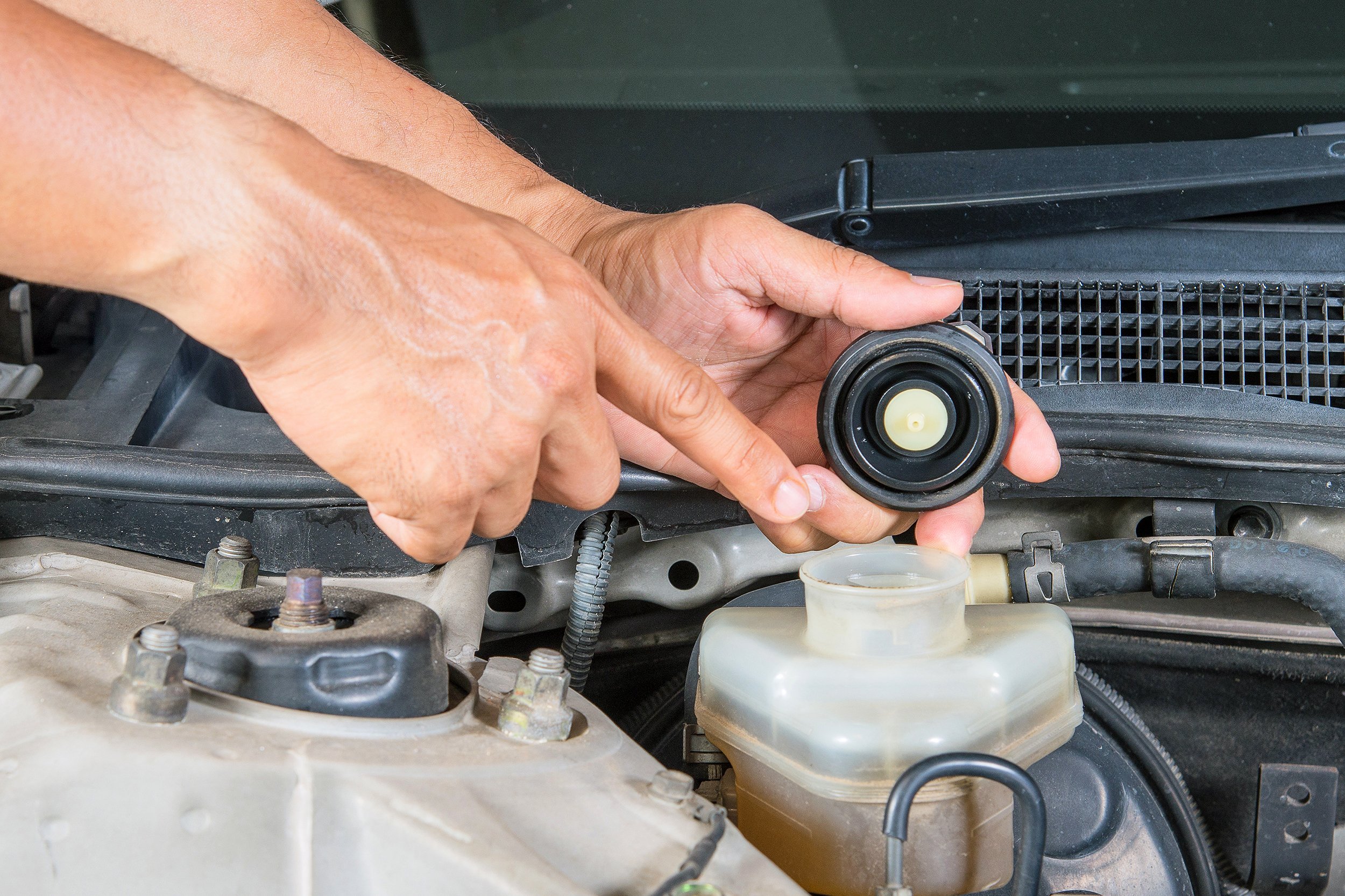 hand pointing to brake fluid inlet under car hood