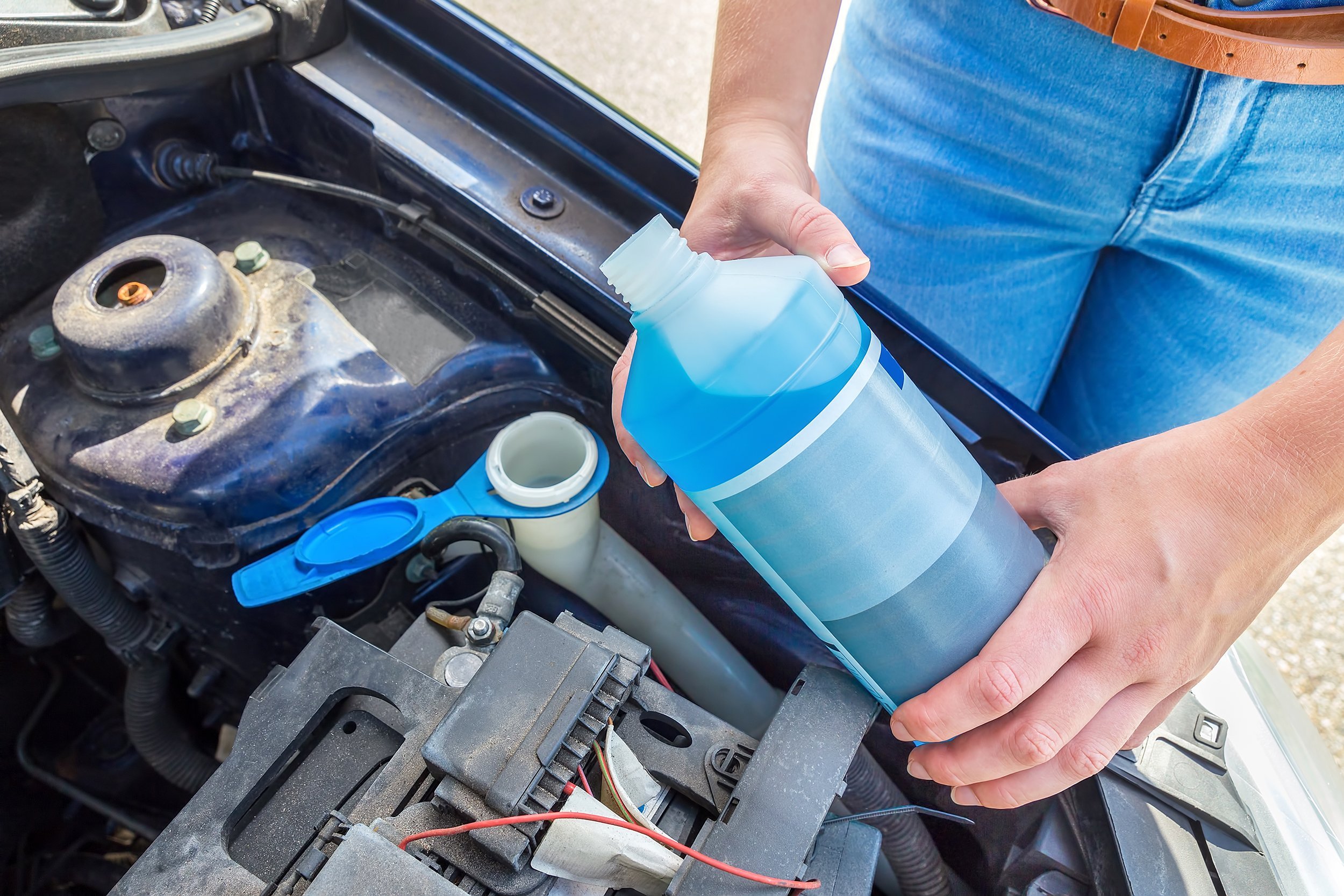 woman filling car reservoir with windshield wiper fluid