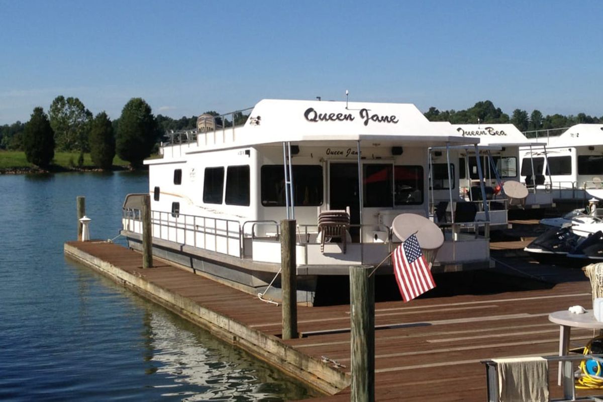 Wooden dock of marina with three white houseboats on Smith Mountain Lake, Virginia, shoreline with fields and trees in the background, on a sunny day