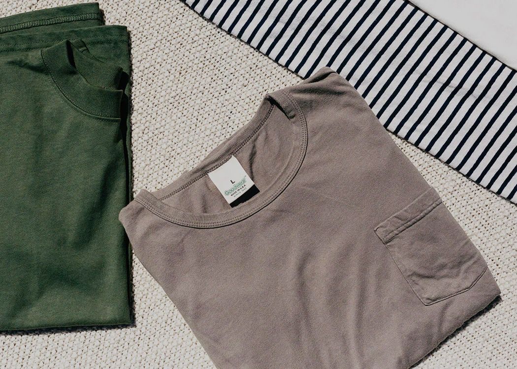 Folded forest green and dark tan t-shirts on a beige woven cloth background from Goodwear USA