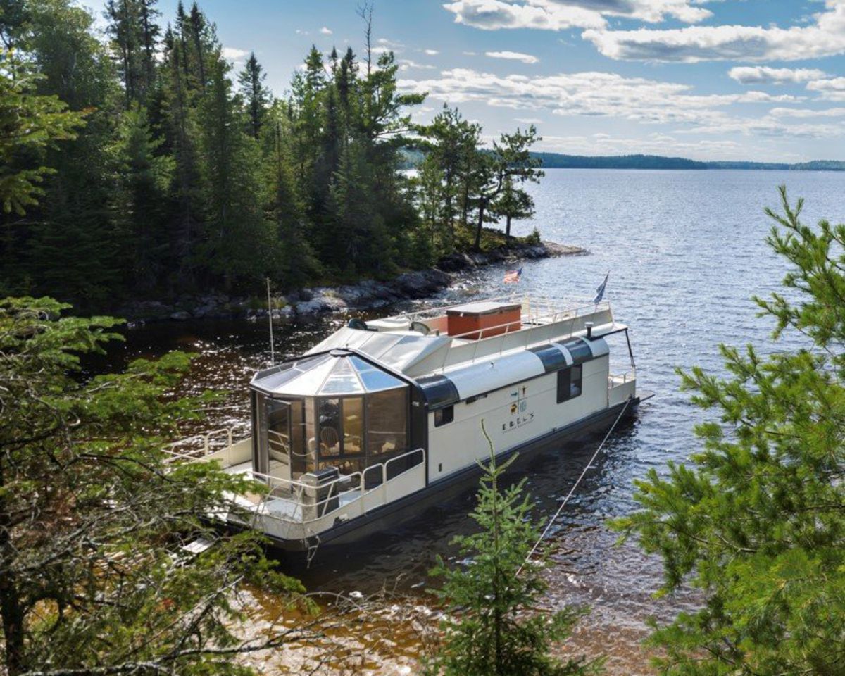 Houseboat docked in Voyageurs National Park, Minnesota, evergreen trees lined the shoreline, with lake in the background on a sunny day