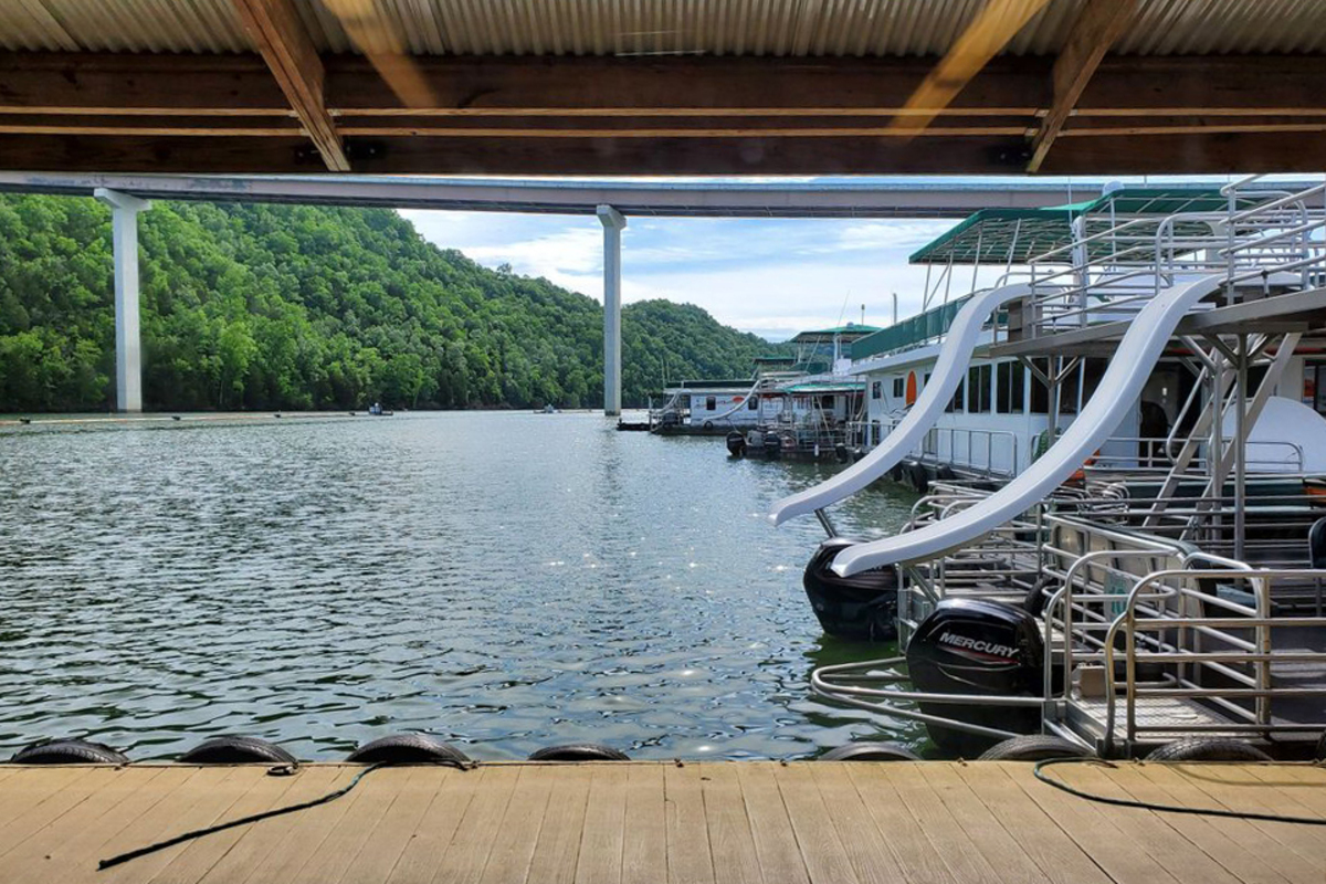 Line of houseboats on the right at the marina on Dale Hollow Lake, Tennessee, as seen from a shaded walkway dock, trees on hills in the background on a sunny day