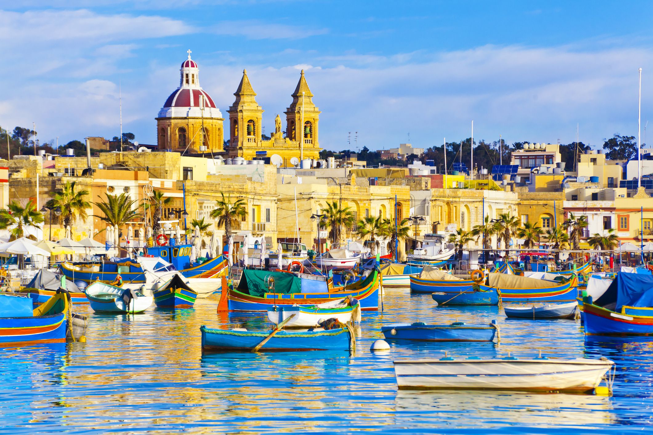 Marsaxlokk Fishing Village, Malta with small, colorful fishing boats on oceanand buildings in the background