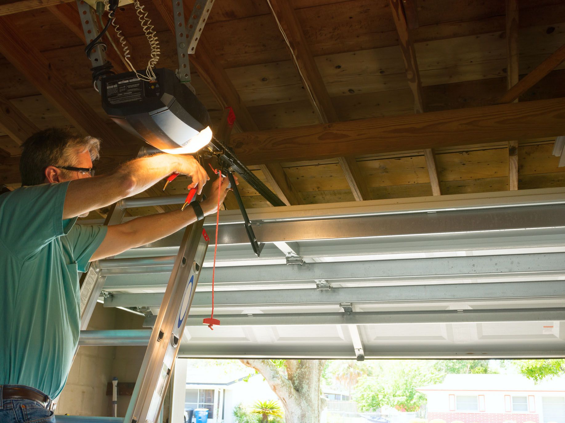 Professional automatic garage door opener repair service technician man working on a ladder at a home residential location making adjustments and fixing it while installing it.