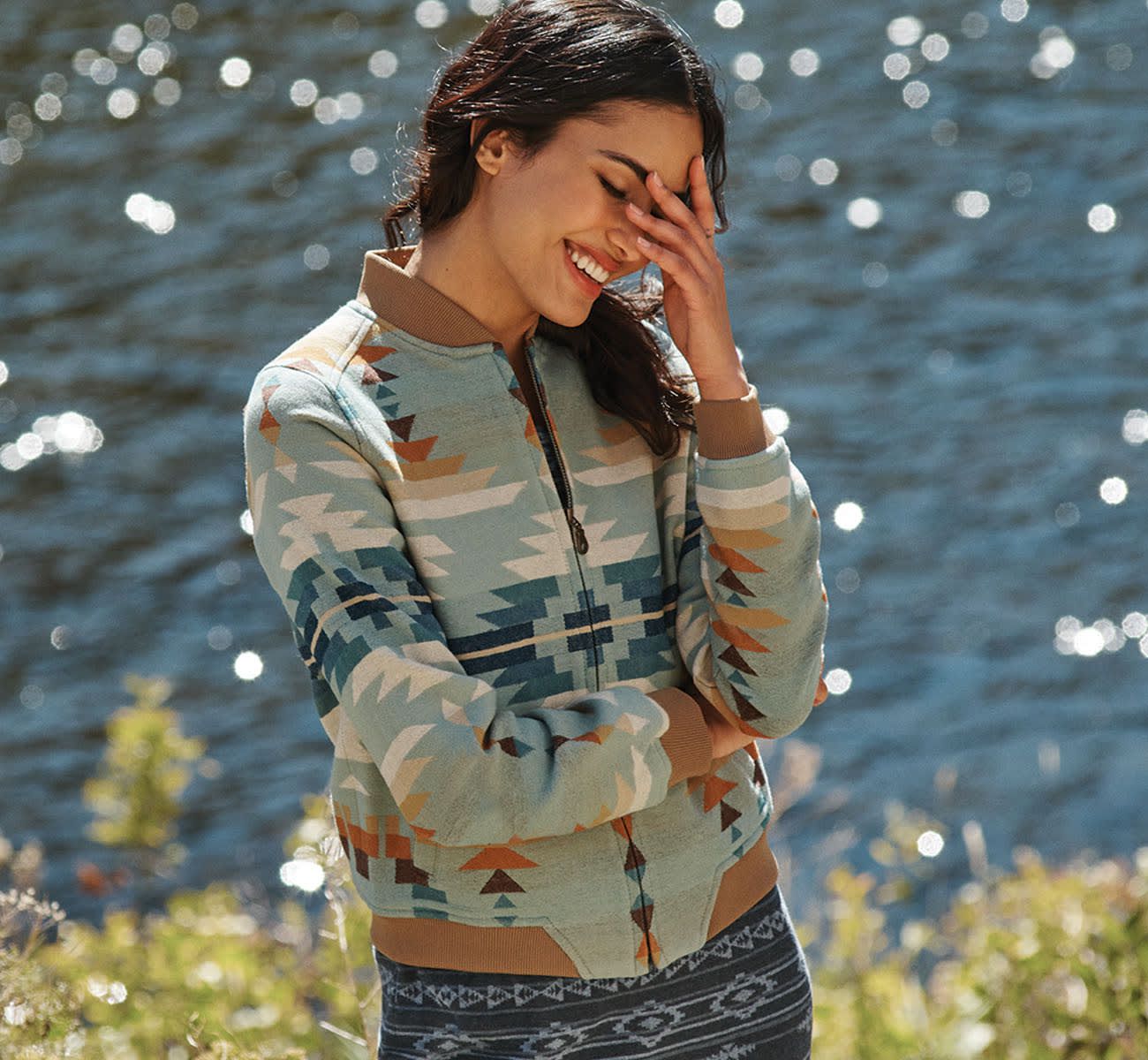 Young woman wearing Pendleton zippered cotton jacket standing in front of a lake with sun reflecting off the water.