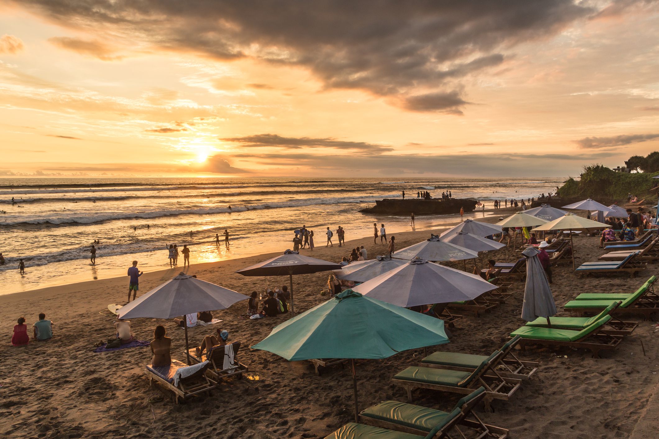 People enjoying the sunset over beach in Canggu, Bali, with umbrellas and beach seating in foreground