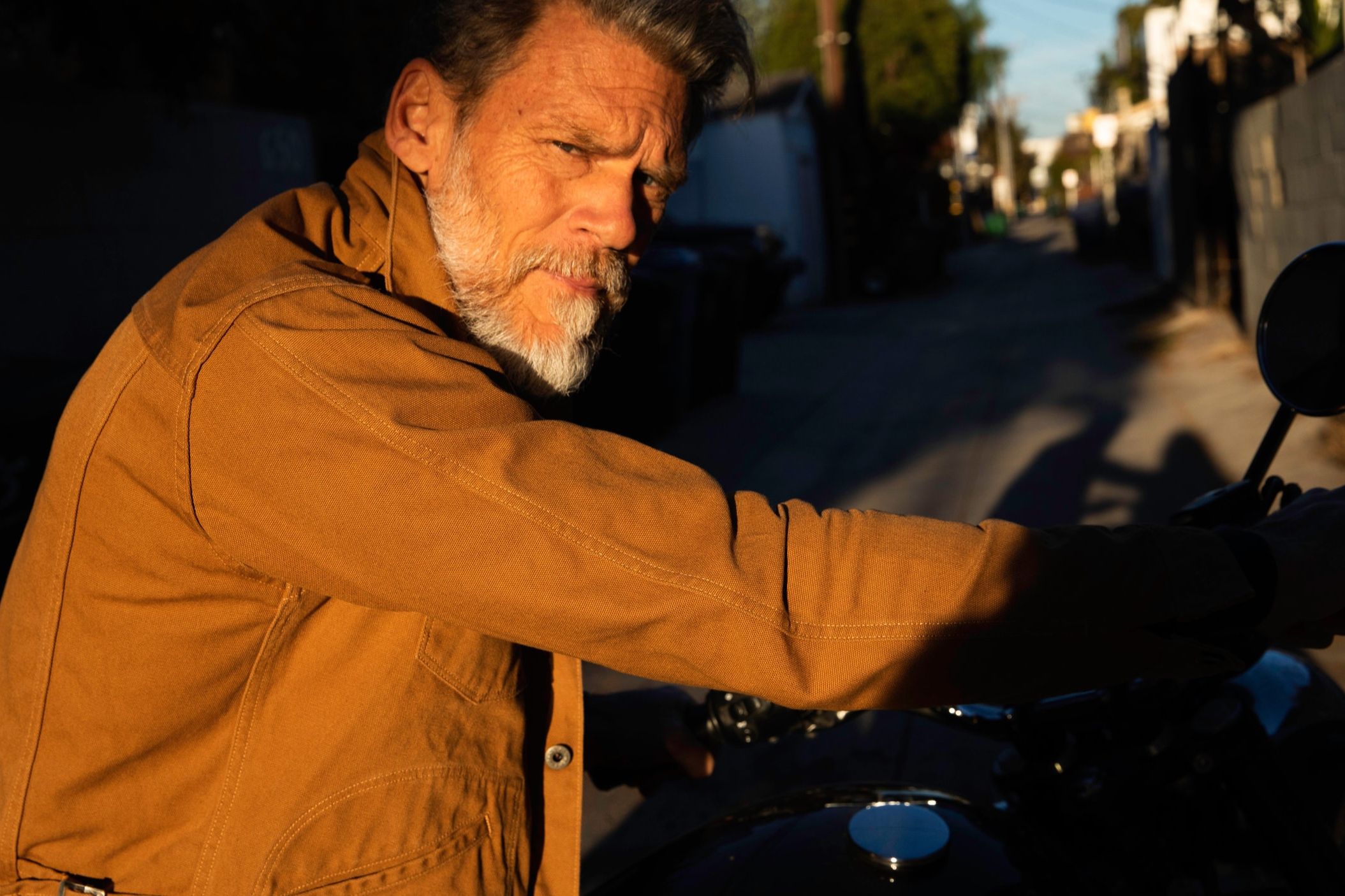 Man with beard on a motorbike wearing a burnt orange cotton jacket from Runabout Goods