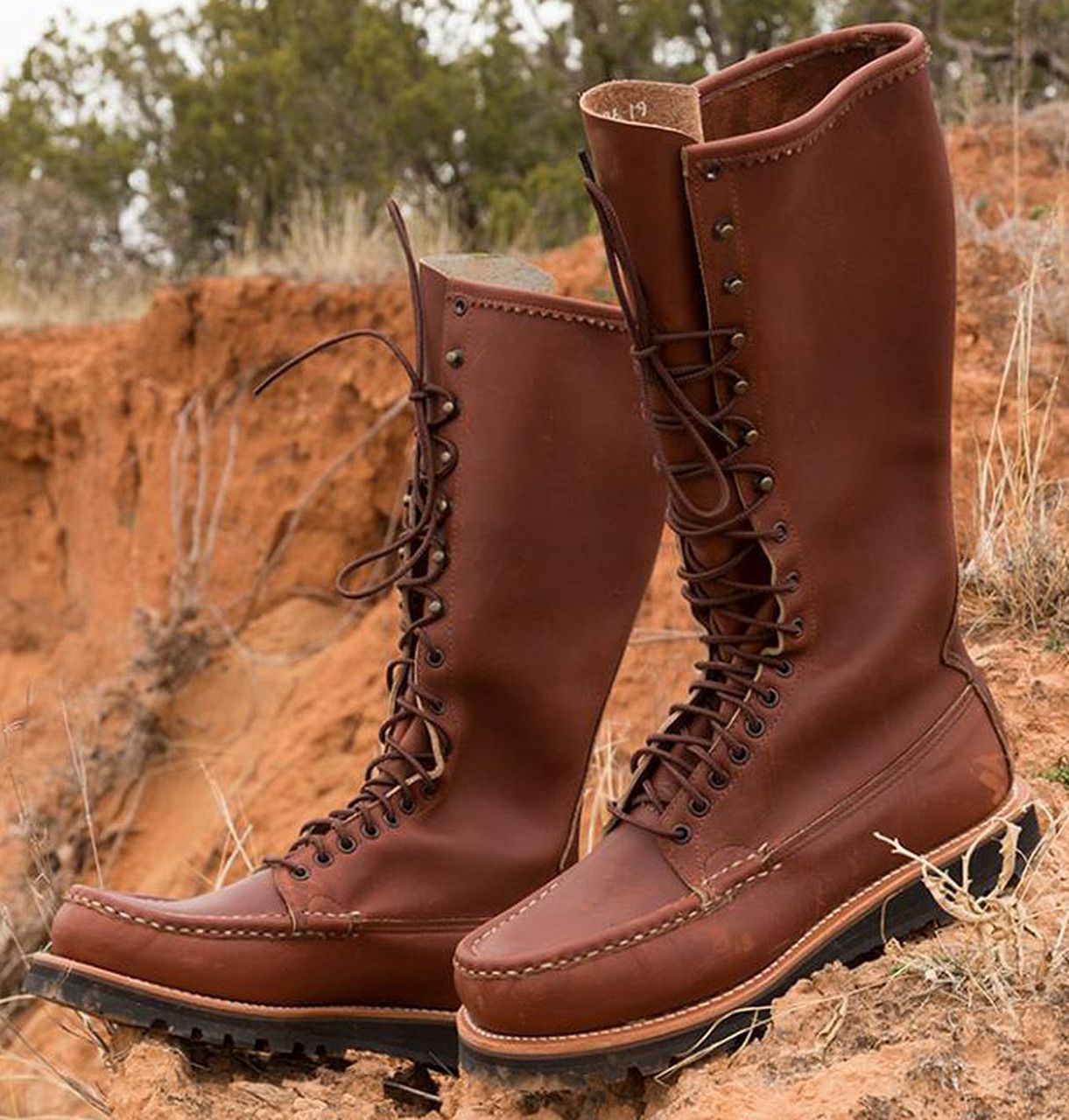 Pair of Russell Moccasin Co. Wyman Boots on dirt cutaway with soil and forest in the background