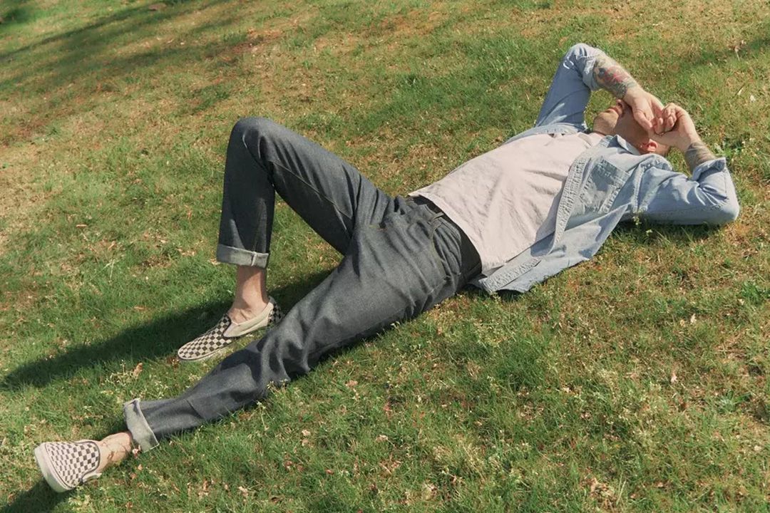 Young man laying on grass covering his eyes from the sun with his wrist while wearing Shockoe Atelier