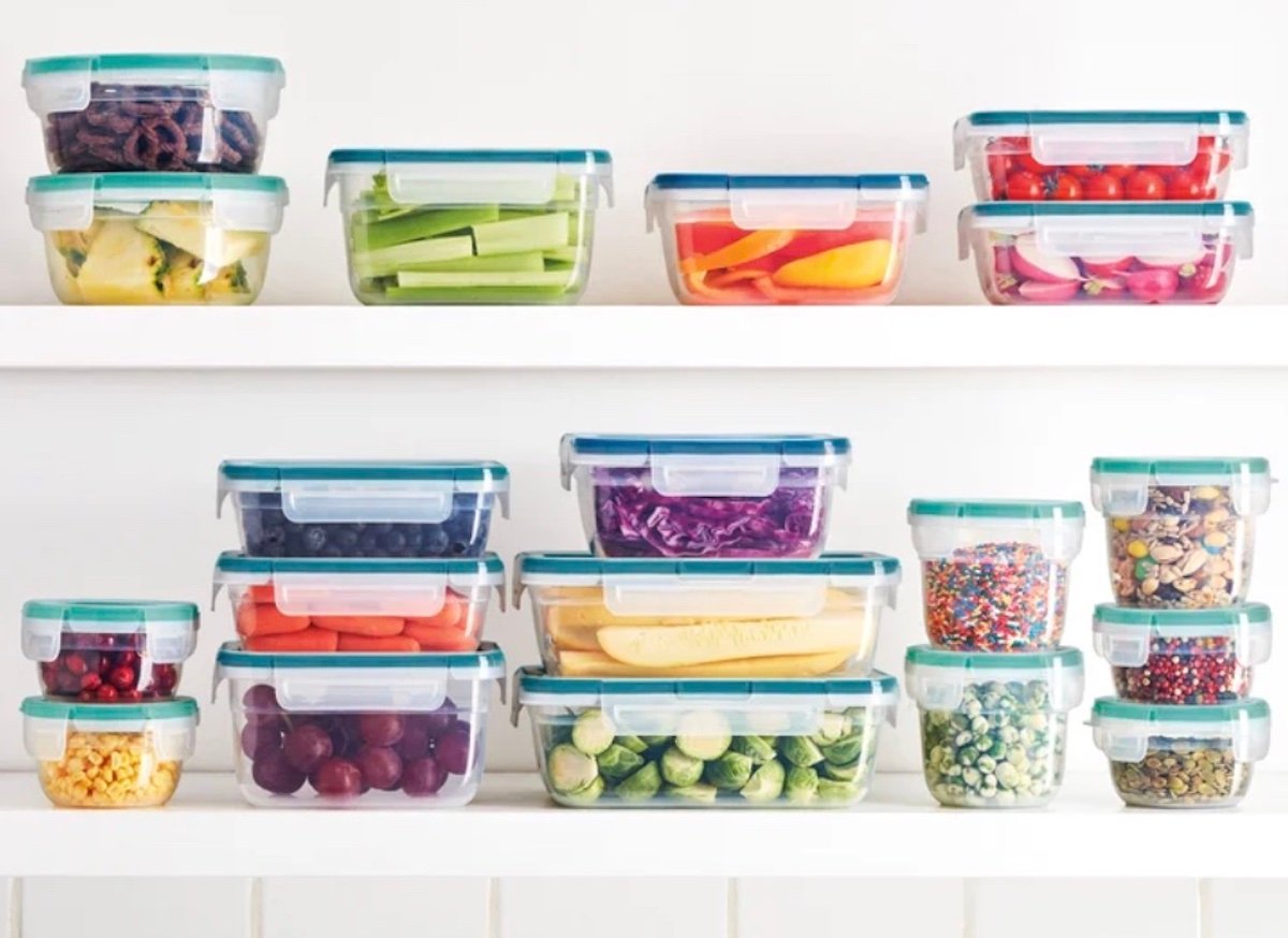 Clear plastic containers filled with colorful fruits, vegetables, and snacks—some of the best Costco finds—are neatly arranged on two white shelves against a white wall.