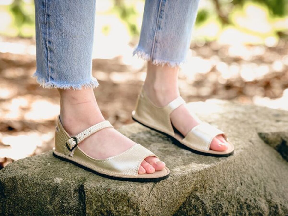 Focus on feet wearing Softstar Adult Solstice Sandal Shiny Platinum while standing on rock with forest background