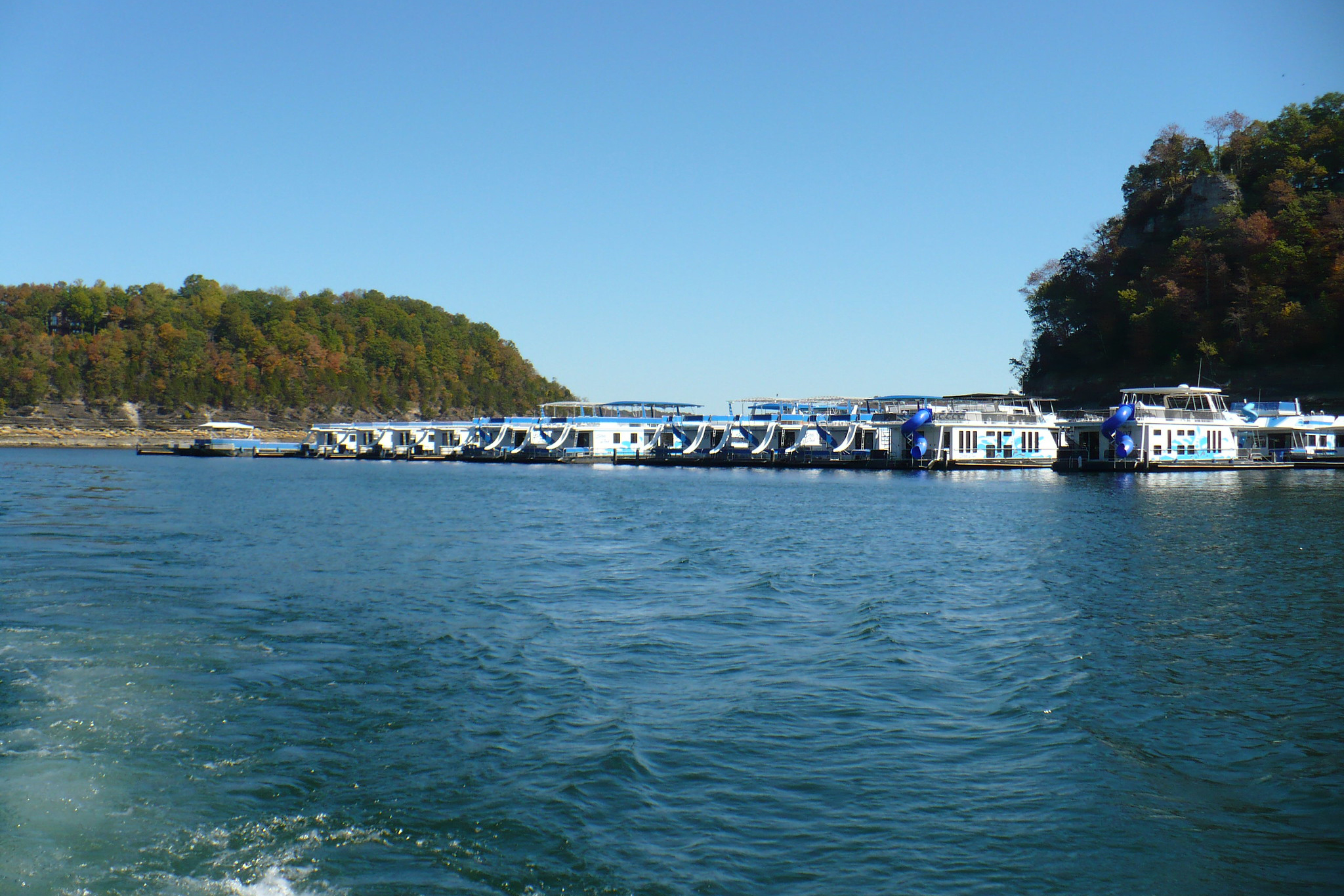Stretch of houseboats docked in the marina of Lake Cumberland, Kentucky in the background, lake as seen from boat in the foreground, on a sunny day