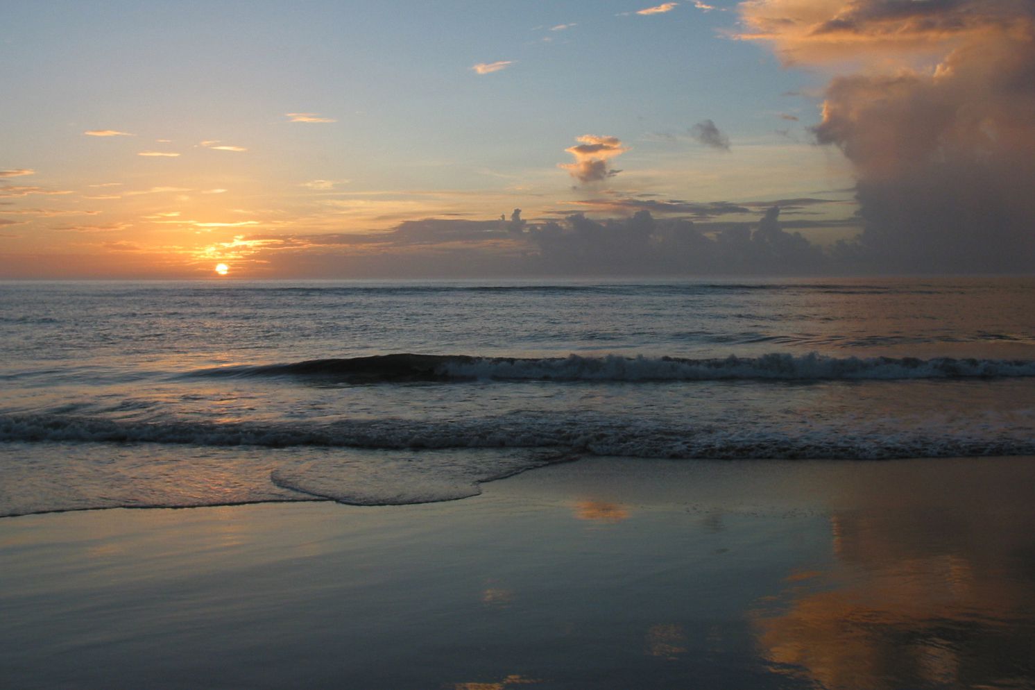 Sunrise along ocean on beach of Duck, North Carolina, reflection of clouds and sky on the wet sand, dramatic orange and purple clouds with a blue sky