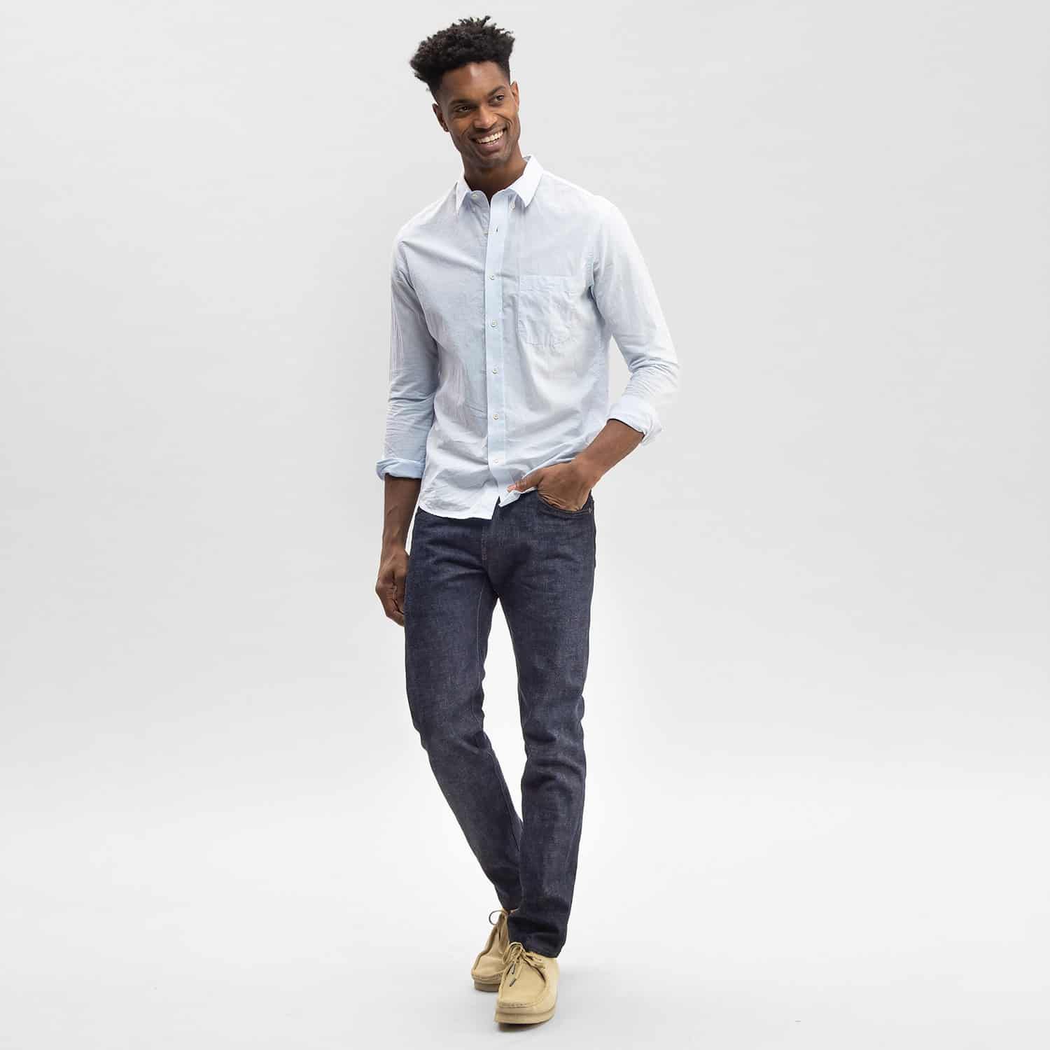 Young man modeling Todd Shelton light blue button down shirt, fitted jeans and beige leather shoes.