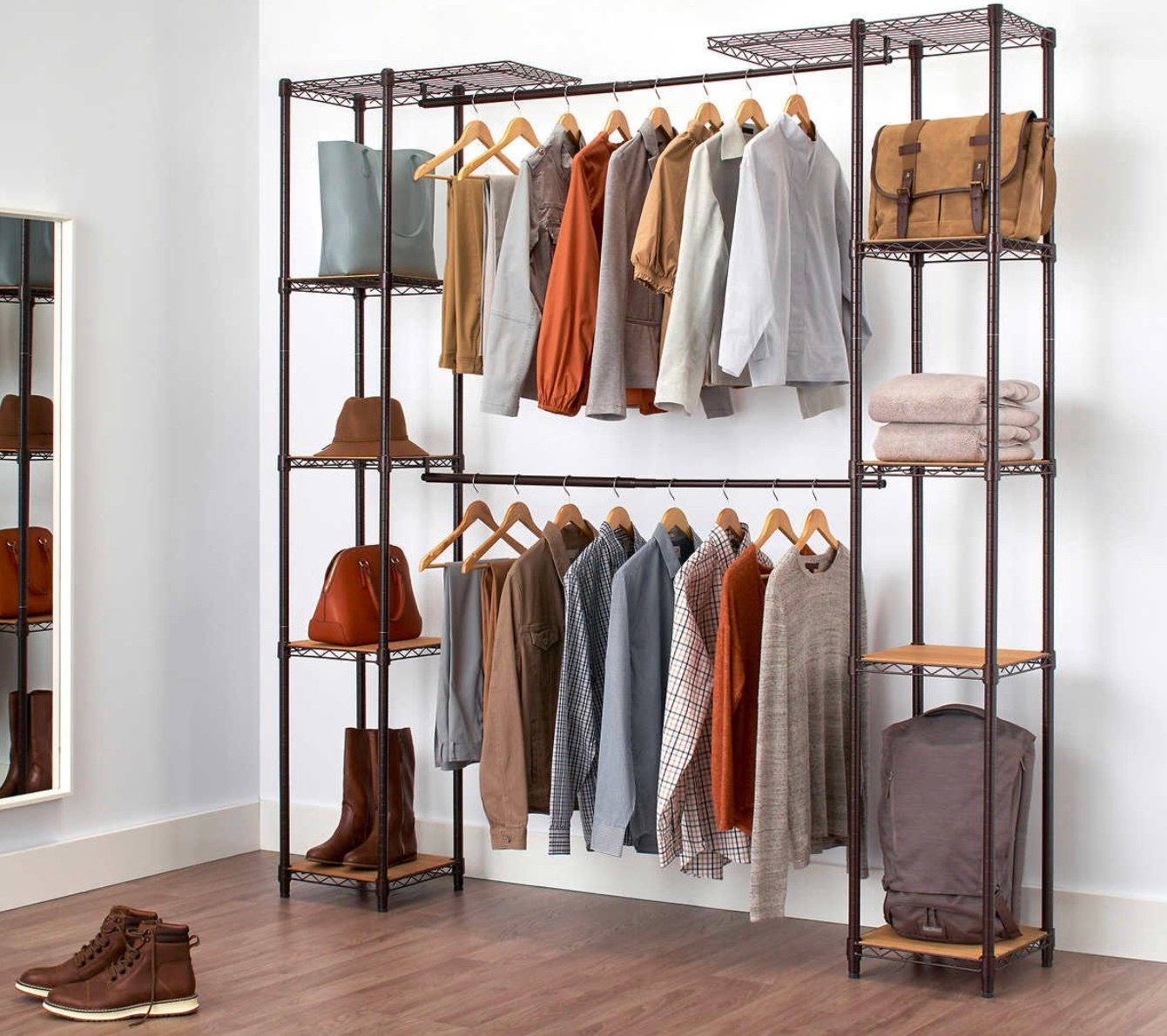 A metal closet organizer, one of the best Costco finds, features shelves and hanging rods for jackets, shirts, sweaters, bags, towels, and boots. It stands against a white wall on a wooden floor with a mirror to the side.