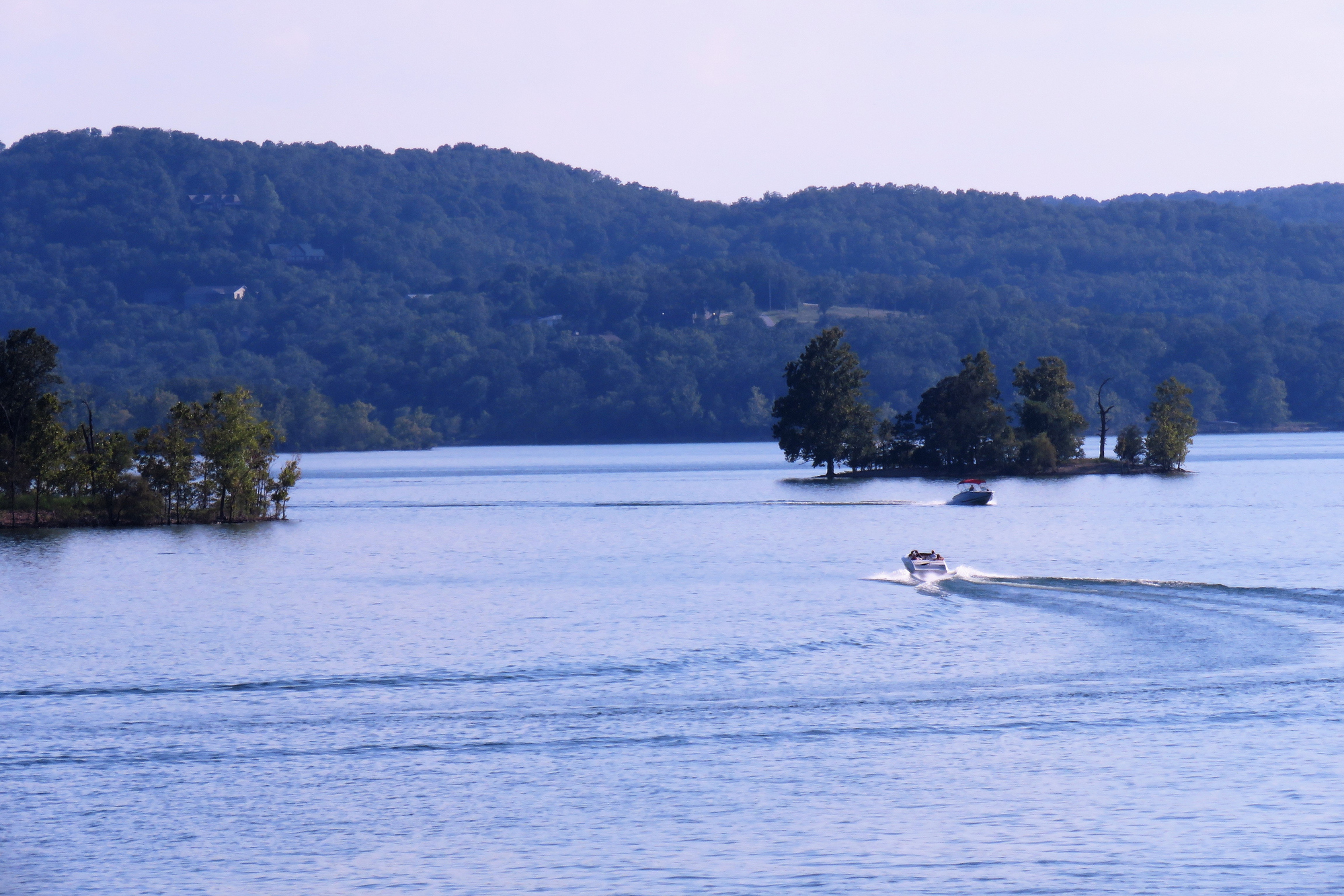 Two boats on water of Table Rock Lake, Missouri, islands of trees scattered with hills in the background, on a cloudy day