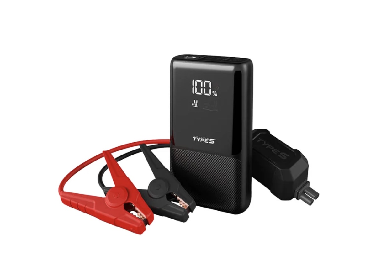 A portable black car jump starter with a digital display, red and black clamps attached by cables, and a charging adapter—one of the best Costco finds—set against a white background.