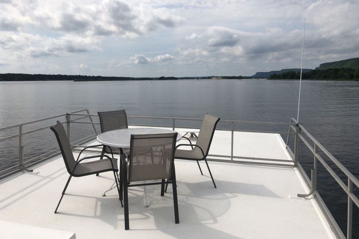 Upper Mississippi River, Alma, Wisconsin, as seen from a houseboat, four chairs and table on top of white deck in the foreground, lake and shoreline in the background on a cloudy day