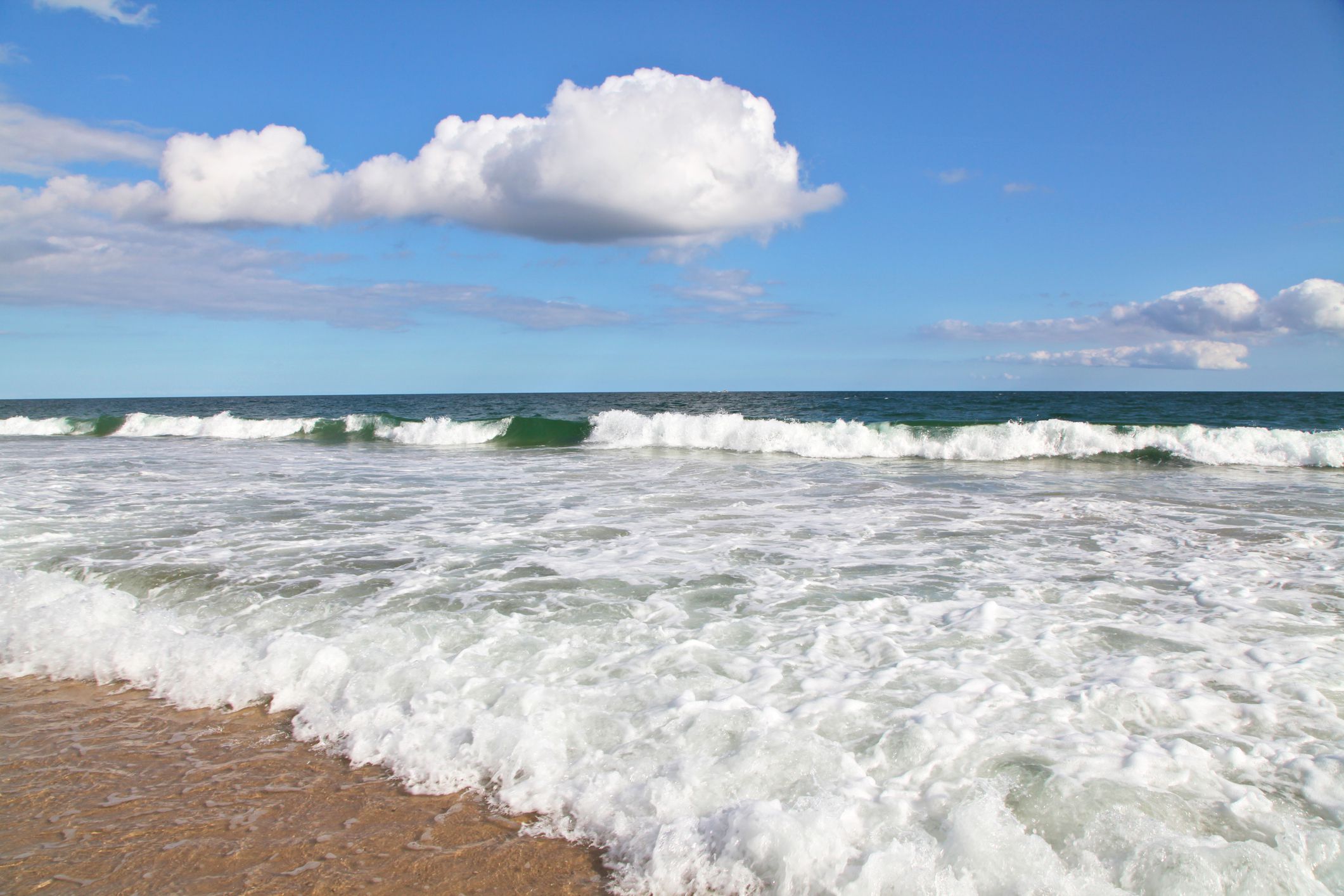 Waves along the beach of Flying Point Beach, Southampton, New York, a blue sky with white and light grey clouds in the background