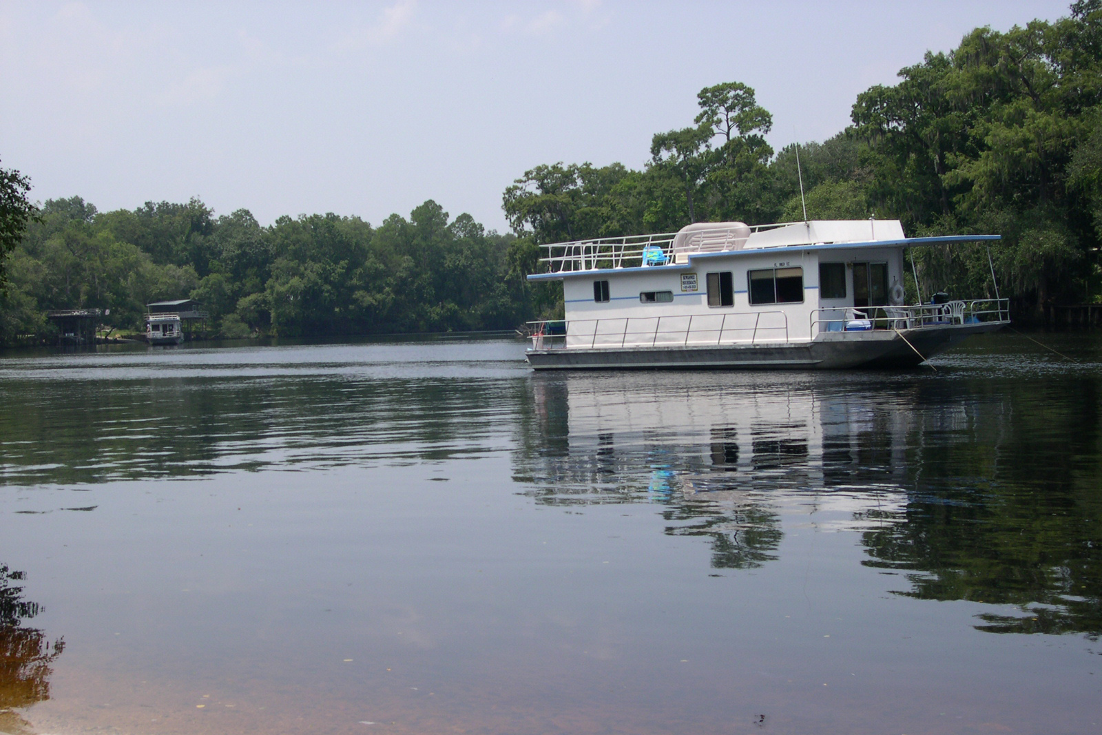 White houseboat on Suwannee River, Florida, shore in the foreground, river surrounded by trees