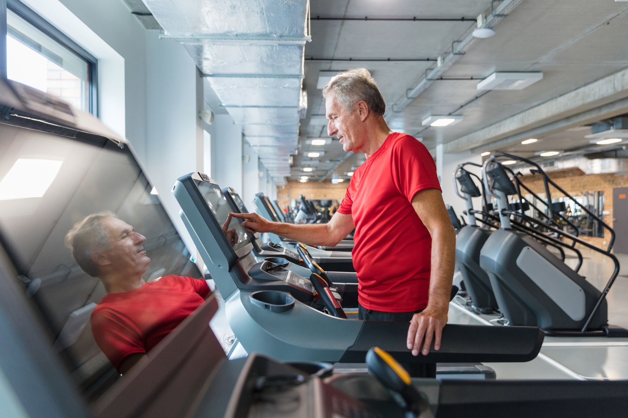 Senior man workout in gym on a exercise machine. Senior man adjusting speed on treadmill at health club.