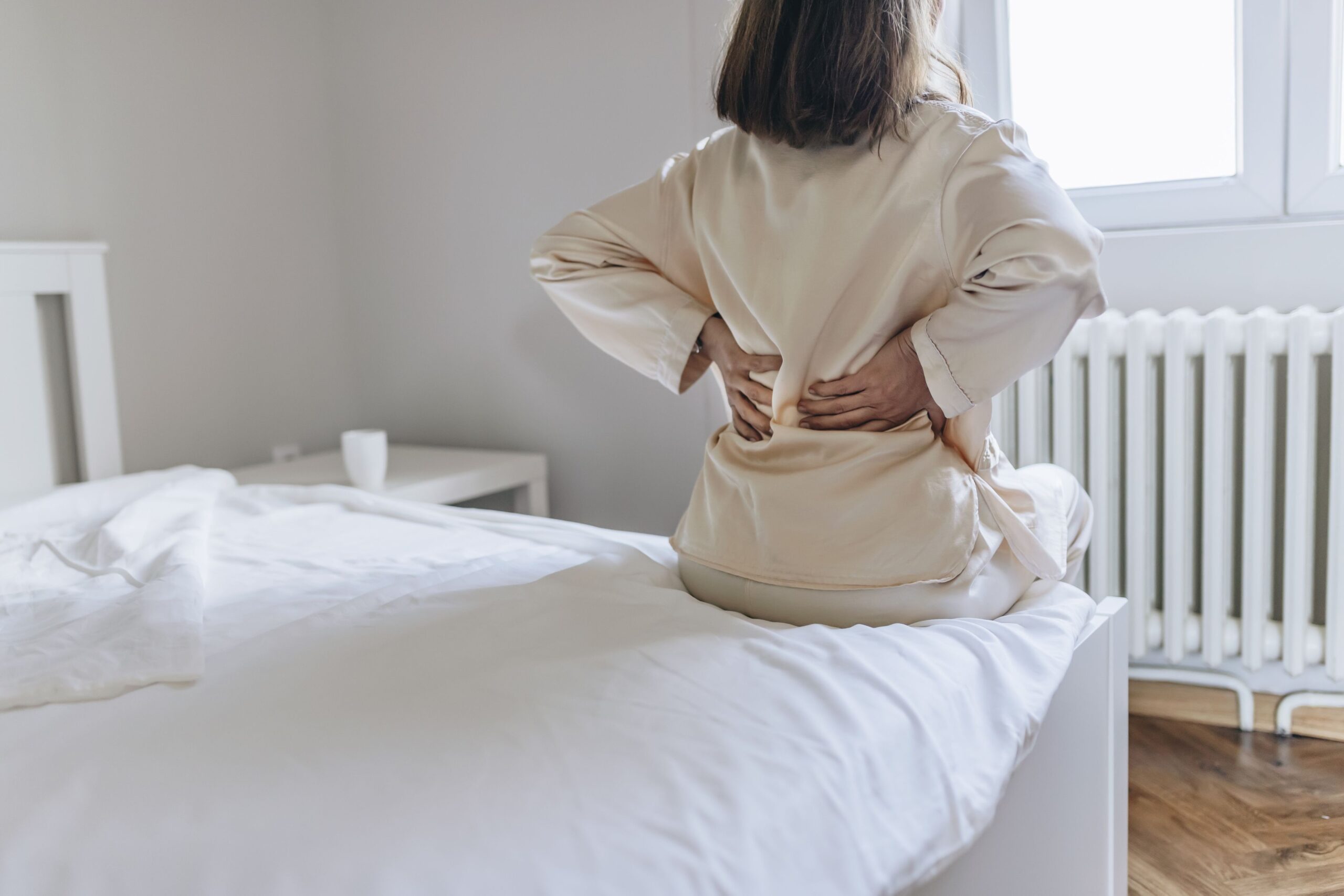 woman holding lower back waking up in bed